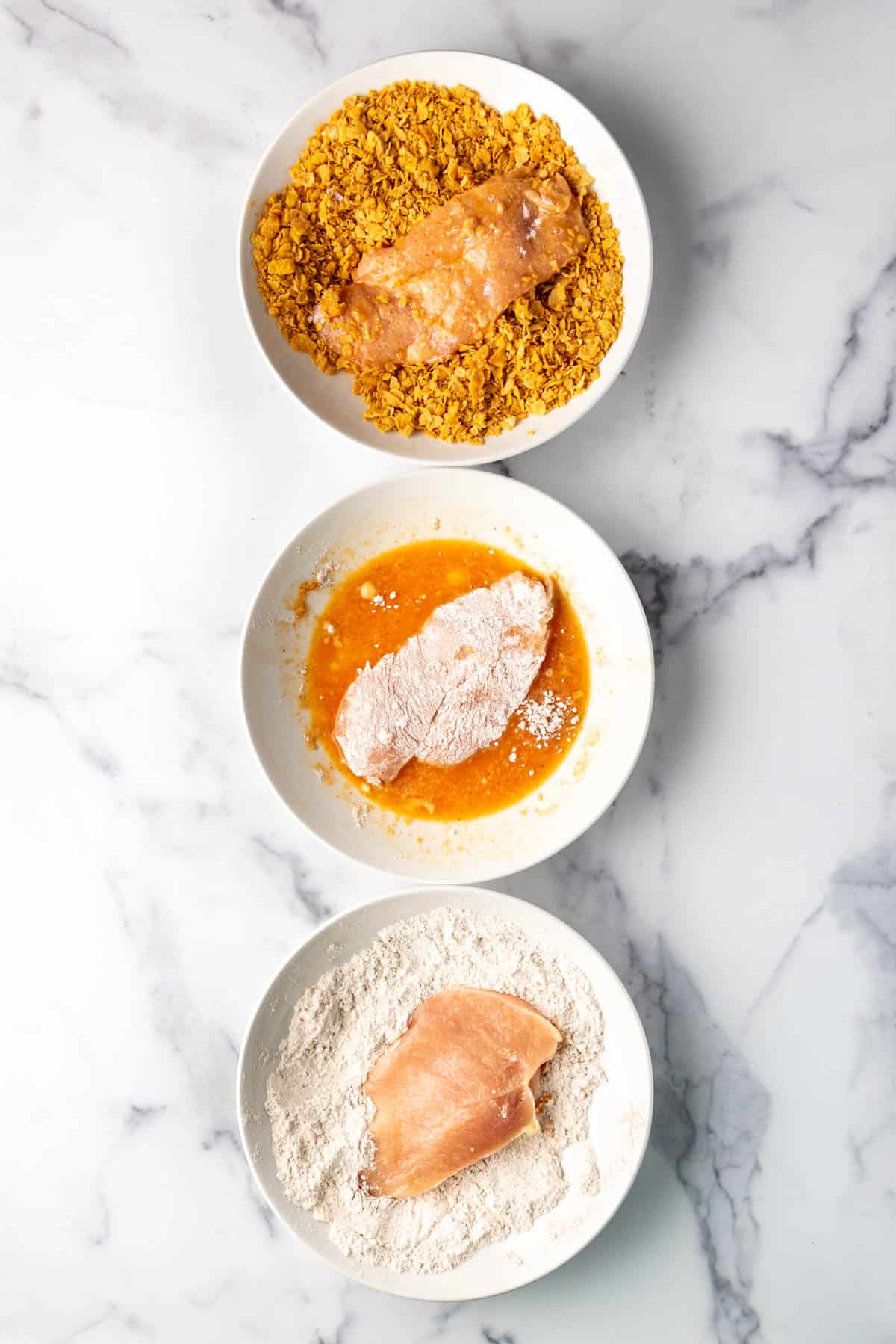 Three bowls with ingredients for dredging cornflake oven fried chicken.