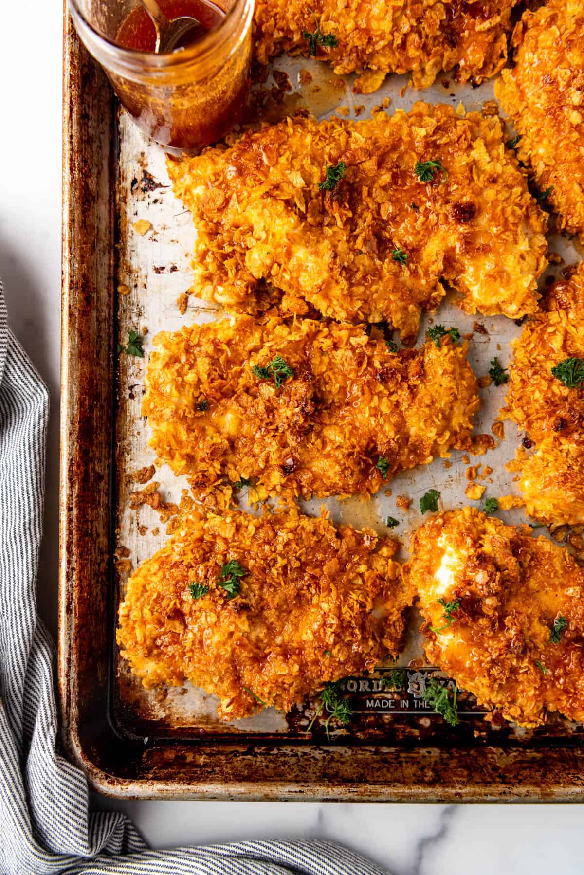 Chicken breasts covered in crushed cornflakes on a baking sheet.