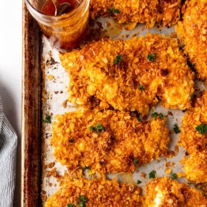 Chicken breasts covered in crushed cornflakes on a baking sheet.