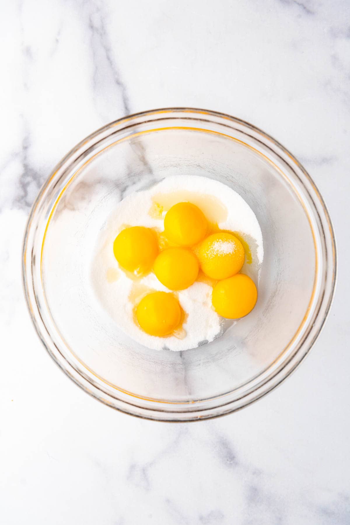 Combining egg yolks and sugar in a glass mixing bowl.