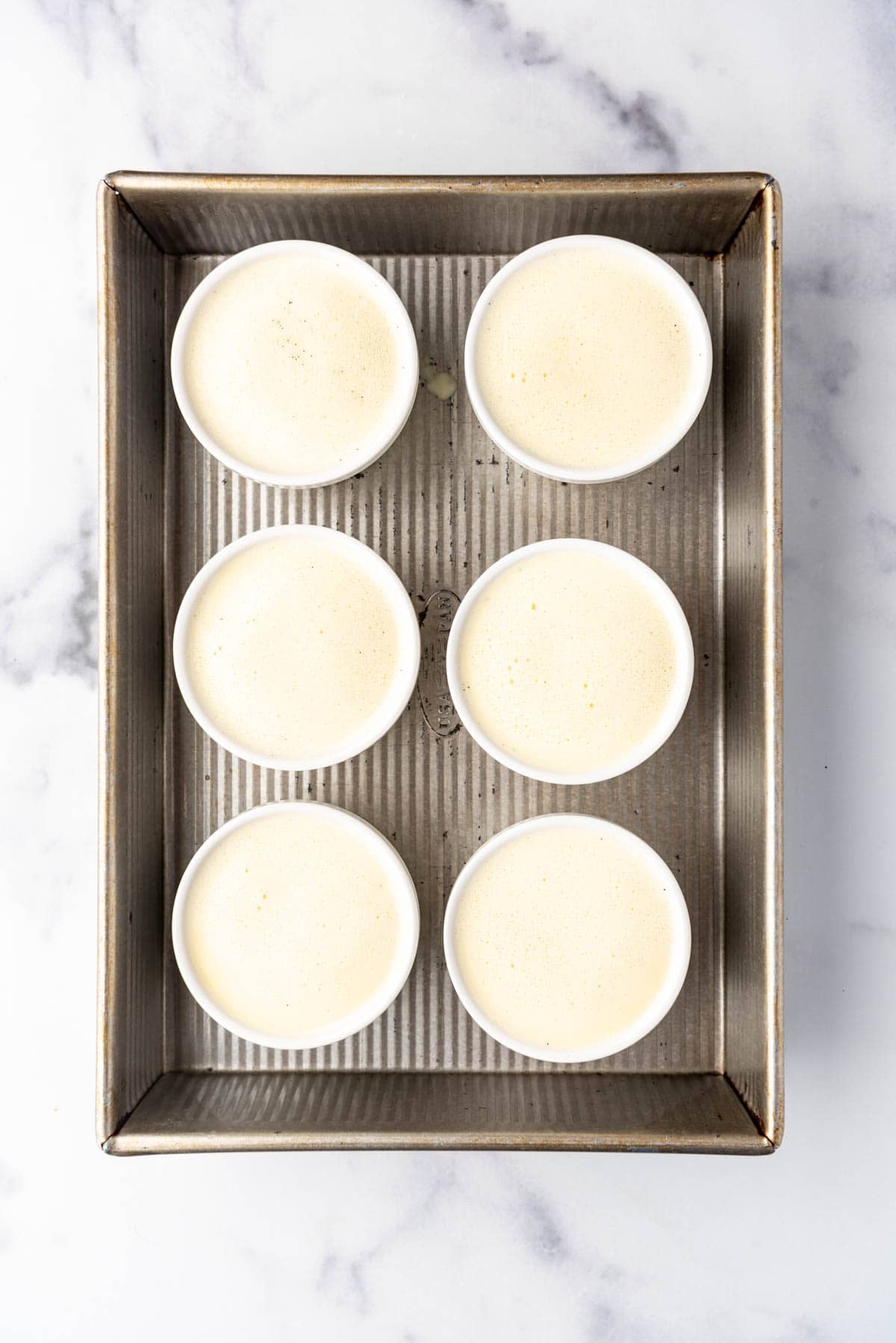 An overhead image of ramekins of cream mixture ready to be baked in a bain marie in the oven to make creme brulee.