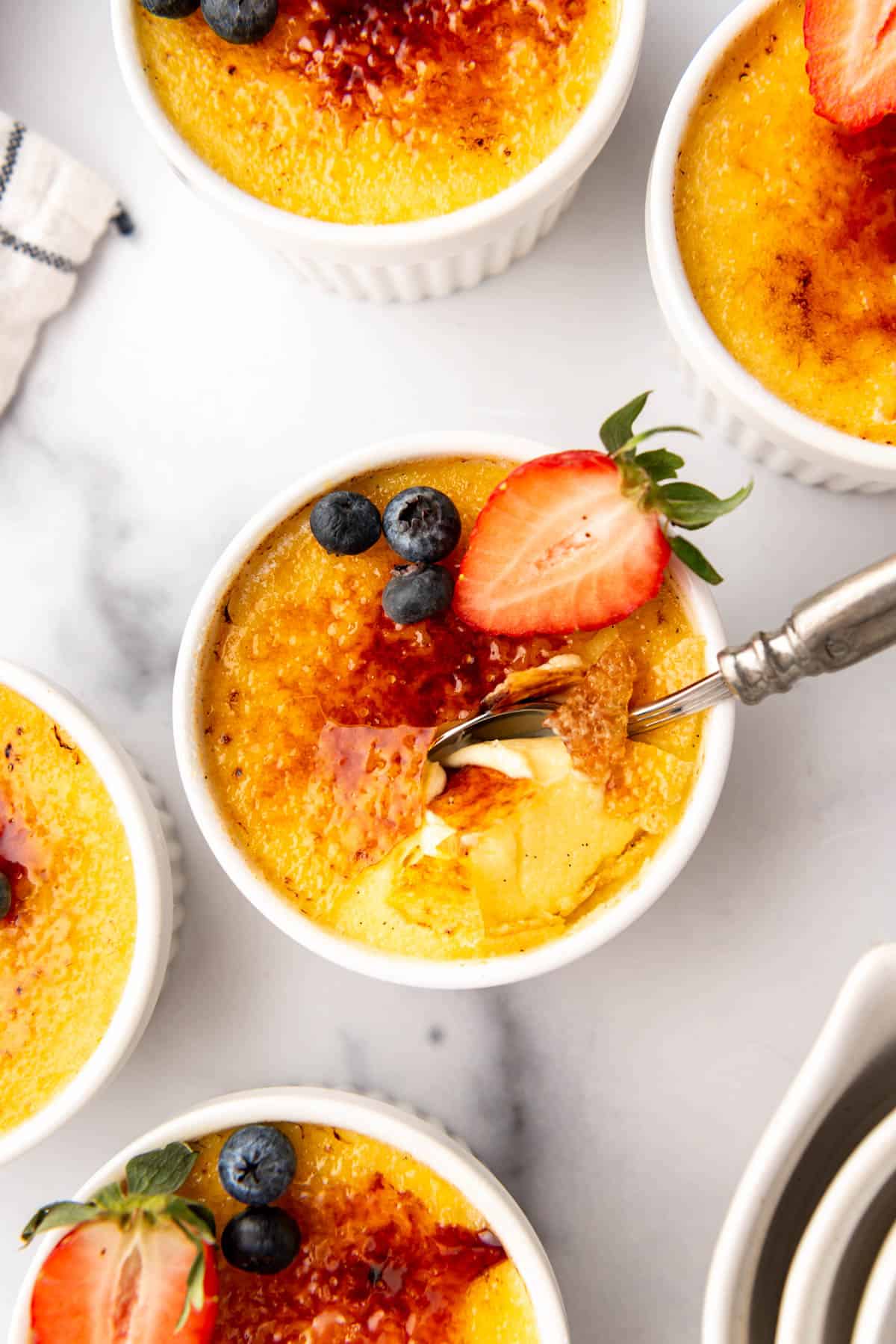 An overhead image of ramekins of creme brulee with a spoon in one.