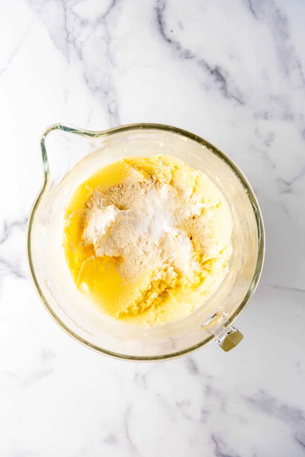 Adding dry ingredients to make a cake batter in a large glass mixing bowl.