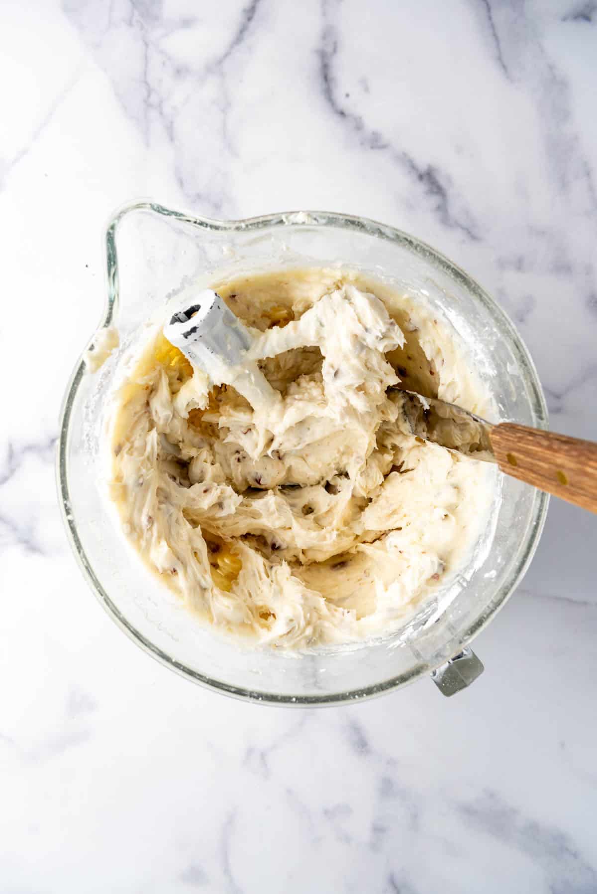 Cream cheese frosting with pecans and toasted coconut in a mixing bowl.