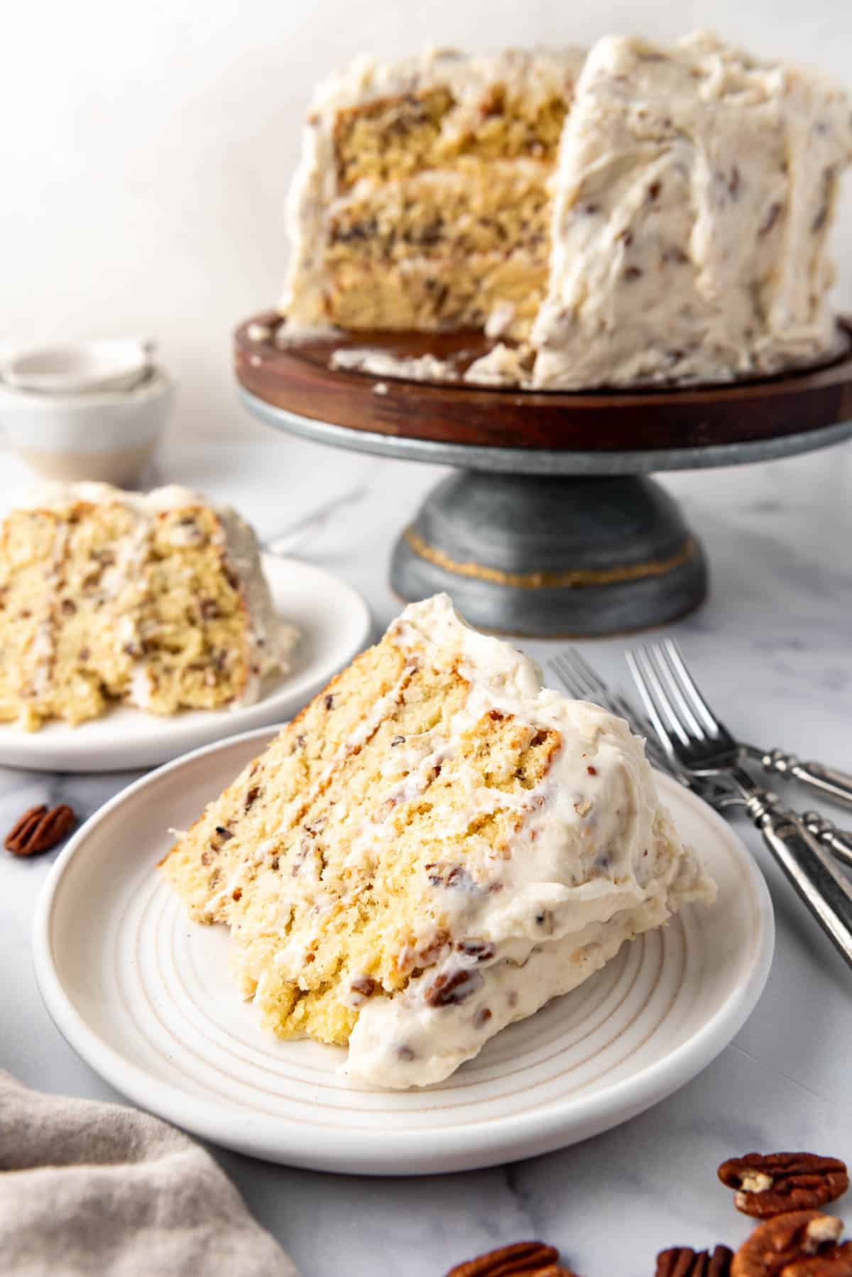 Slices of homemade Italian cream cake on plates in front of the rest of the cake on a cake stand.