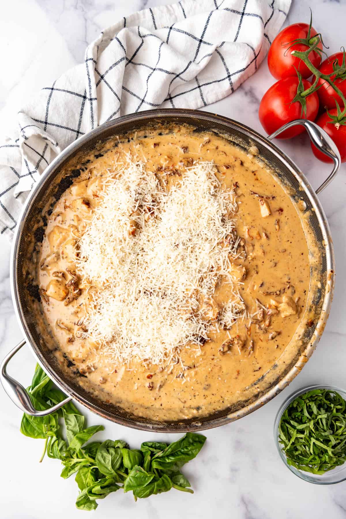 Adding freshly grated parmesan to a sauce in a large skillet.