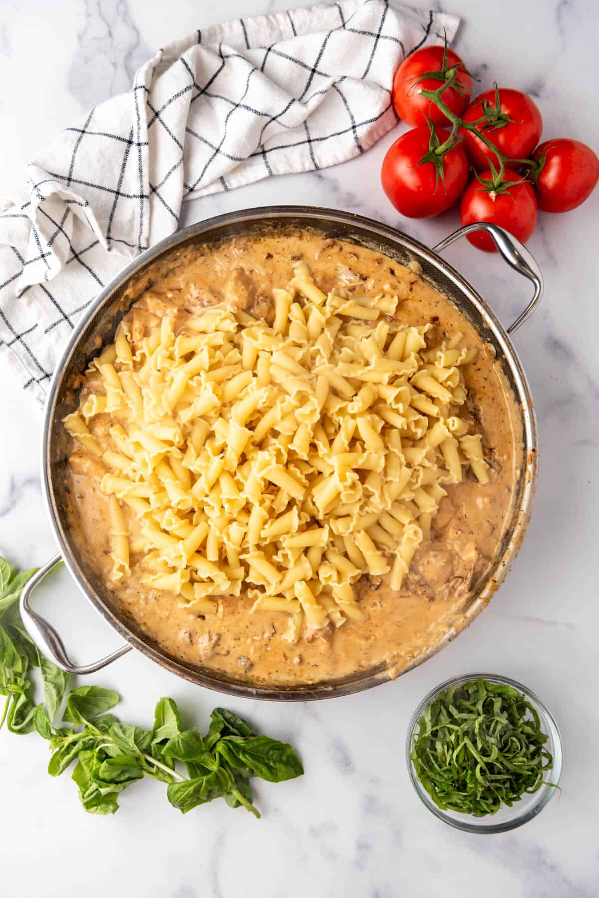 Adding cooked and drained pasta to a sauce in a large pan.