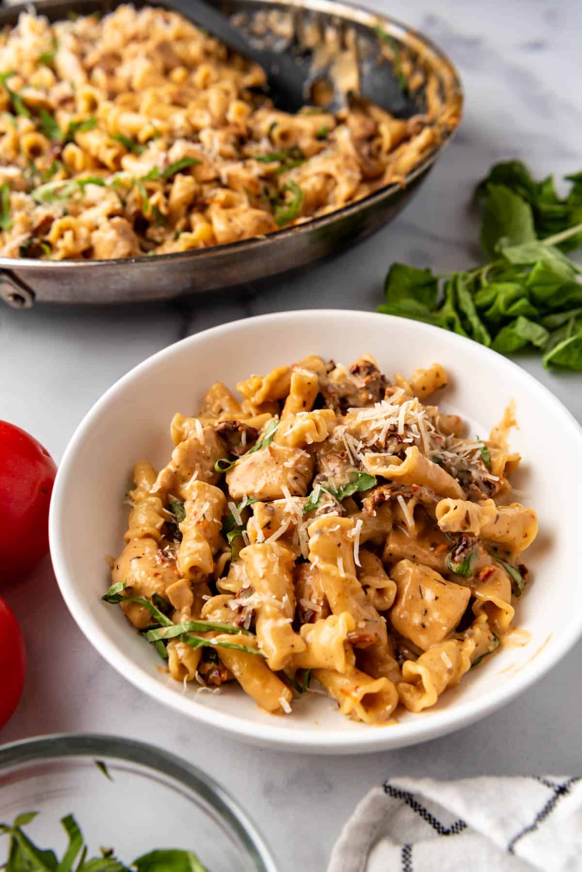 A white bowl of marry me pasta in front of the larger pan of pasta.