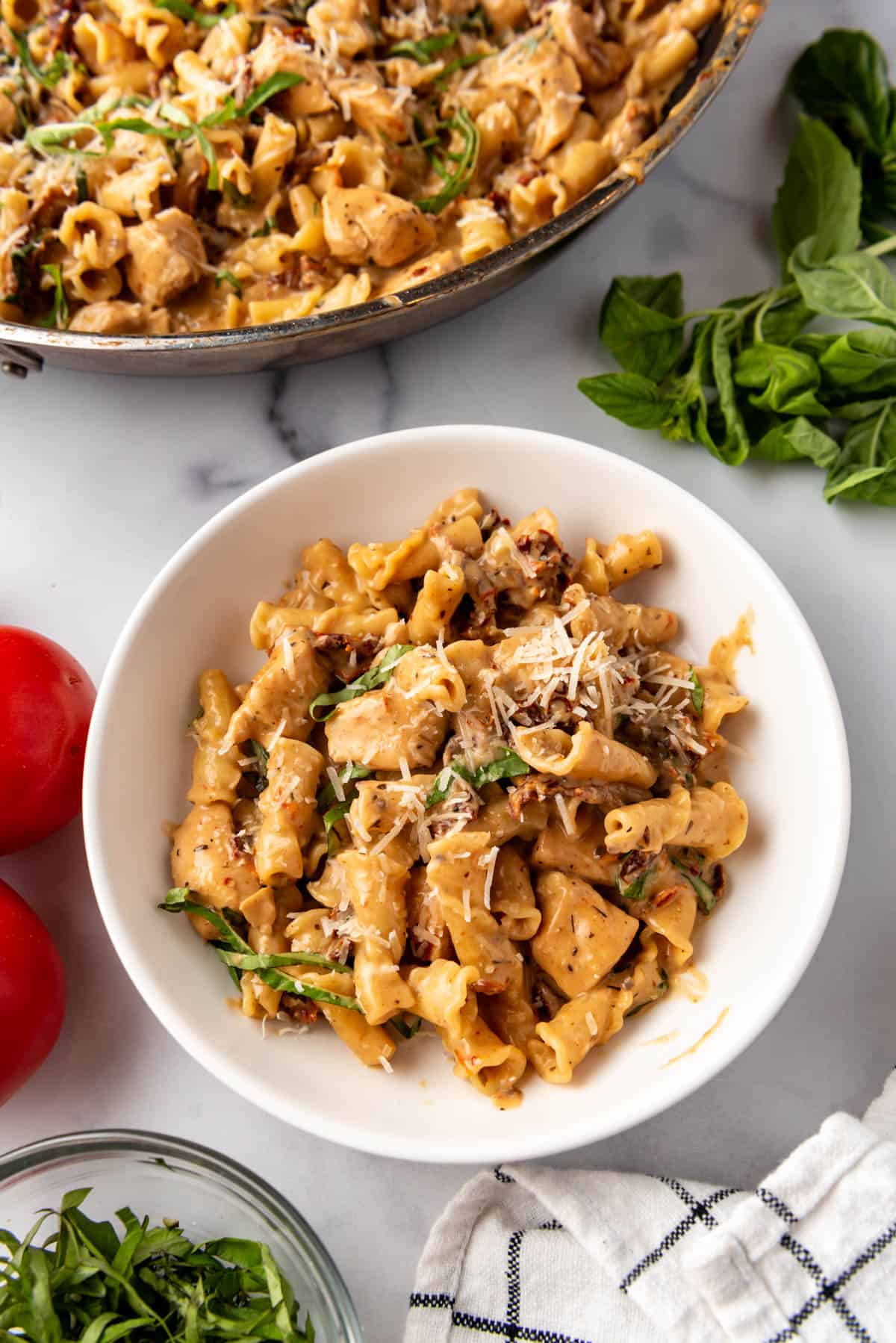 An image of a bowl of marry me chicken pasta next to a larger pan of the pasta.