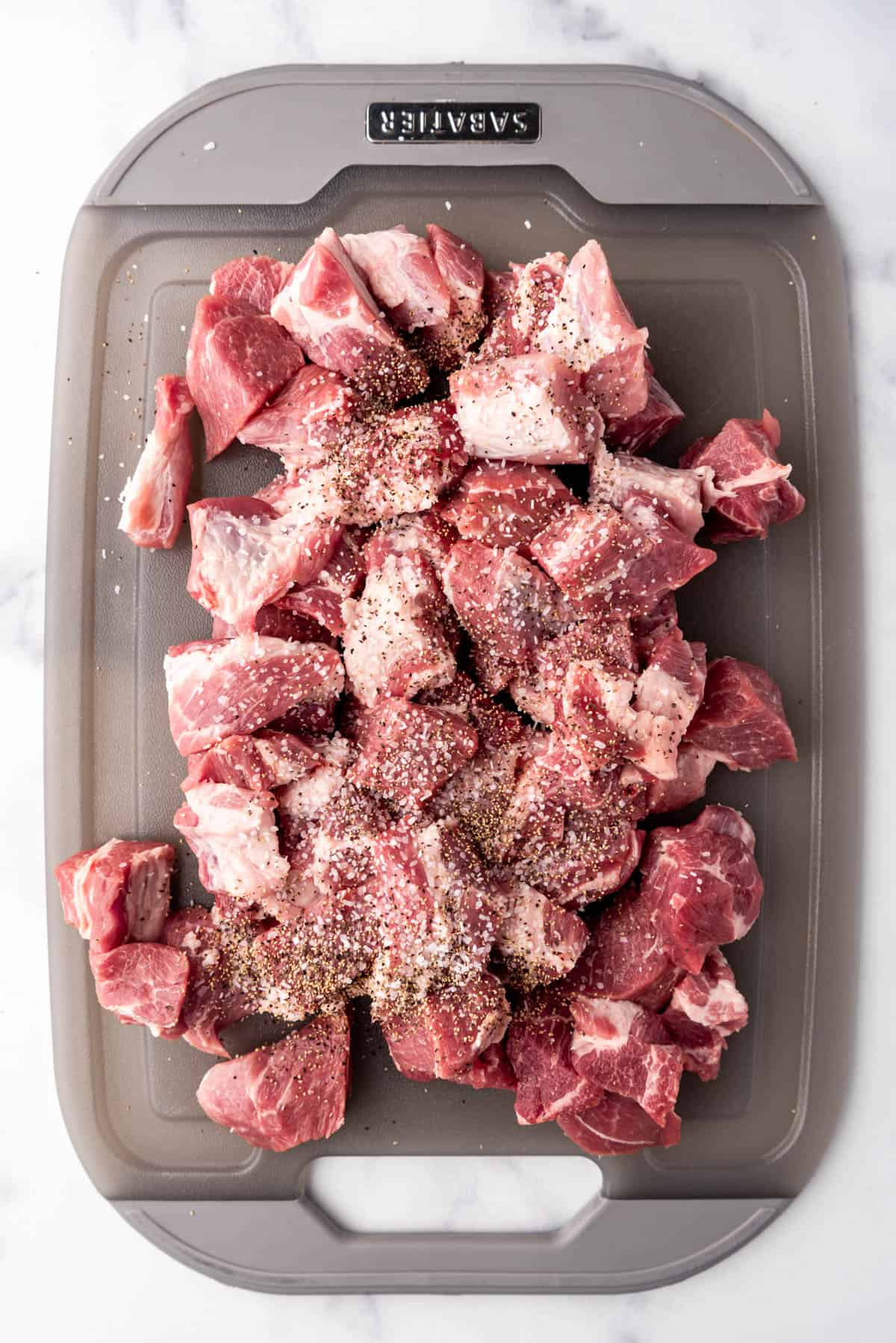 Seasoning chunks of pork butt with salt and pepper.