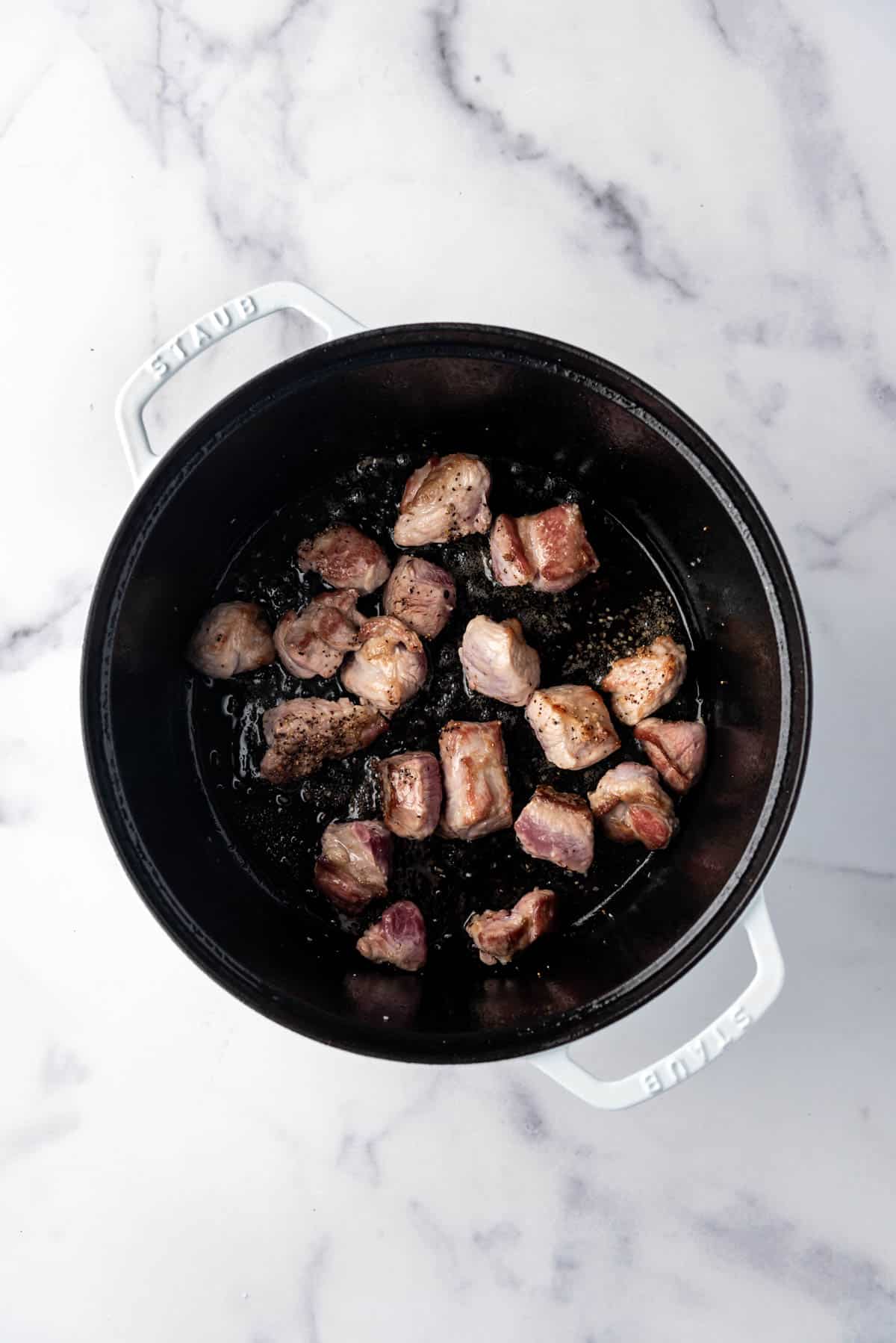 Saisie de morceaux de porc assaisonnés dans une grande cocotte.