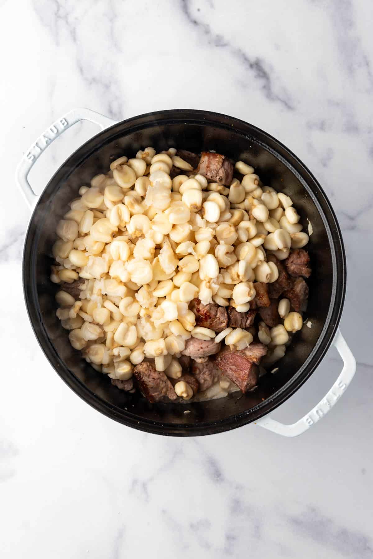 Adding soaked hominy to a large dutch oven.