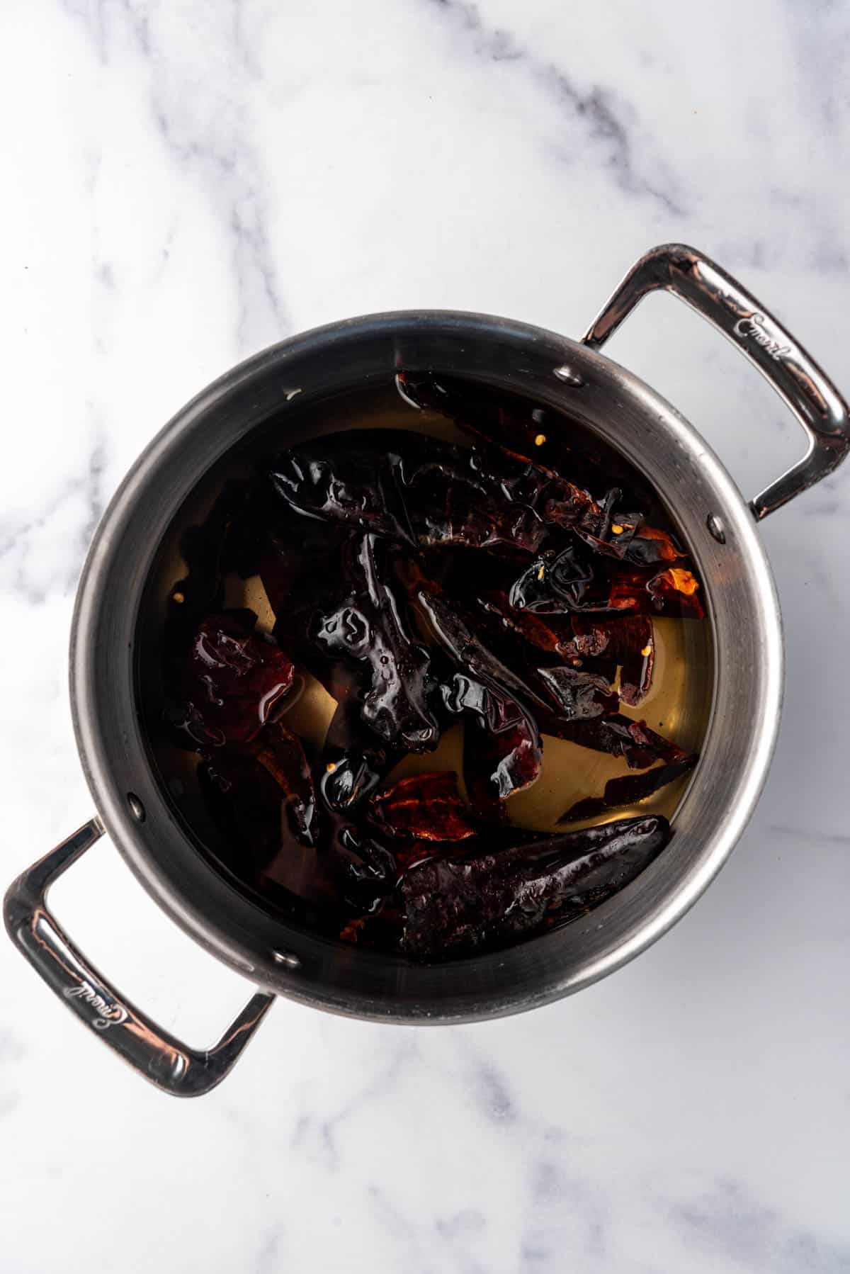 Dried chiles soaking in hot water in a large pot.