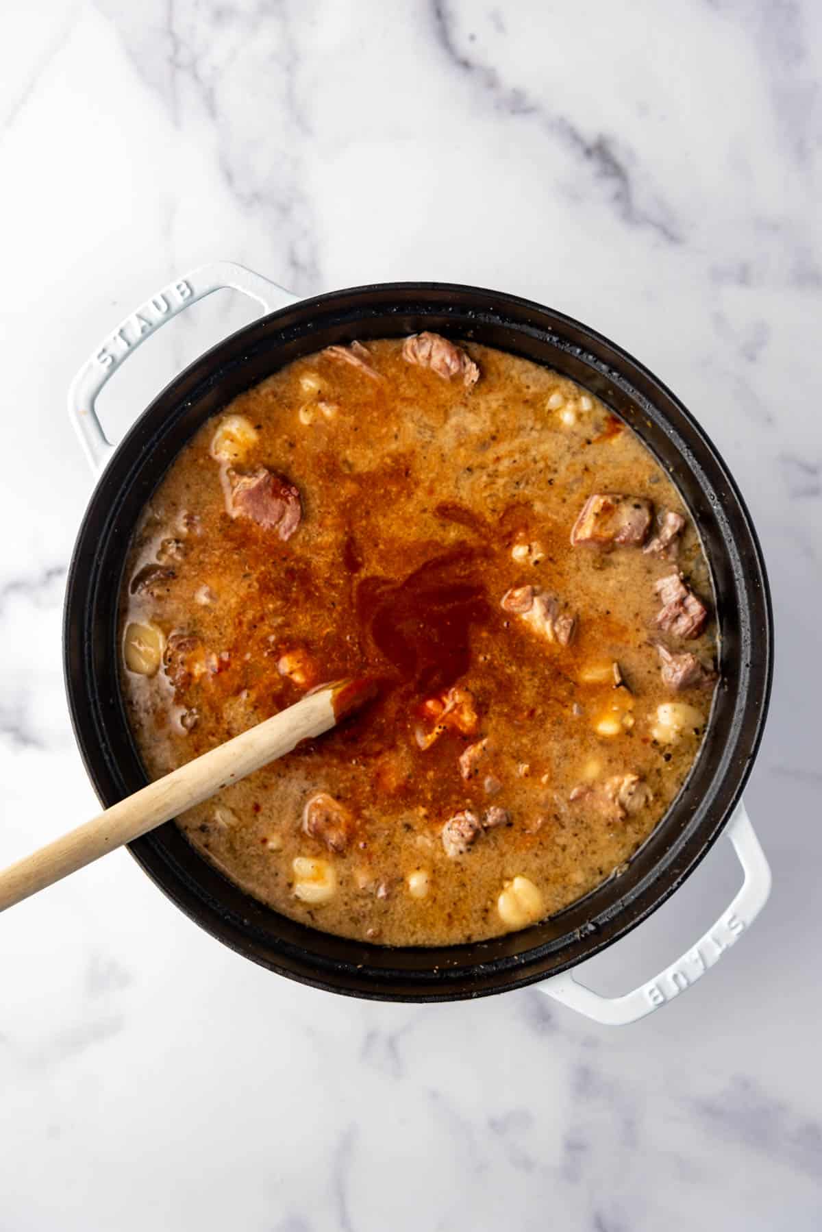 Adding chili puree to a large pot of posole.