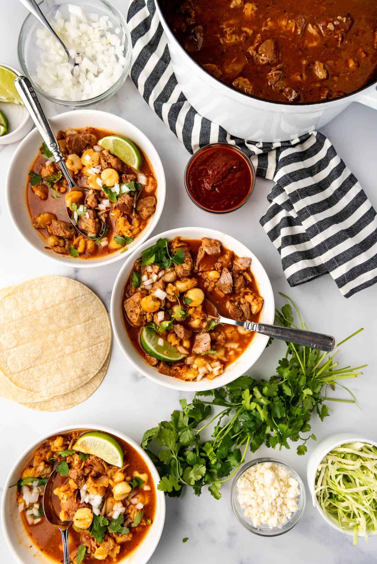 An overhead image of bowls of posole with toppings nearby.