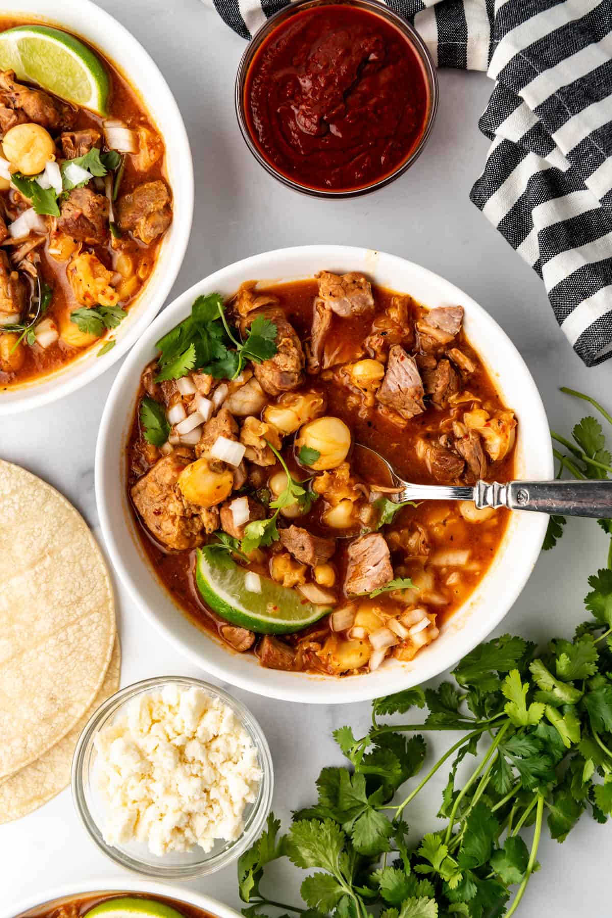 An overhead image of a bowl of New Mexico posole with pork and red chili sauce.