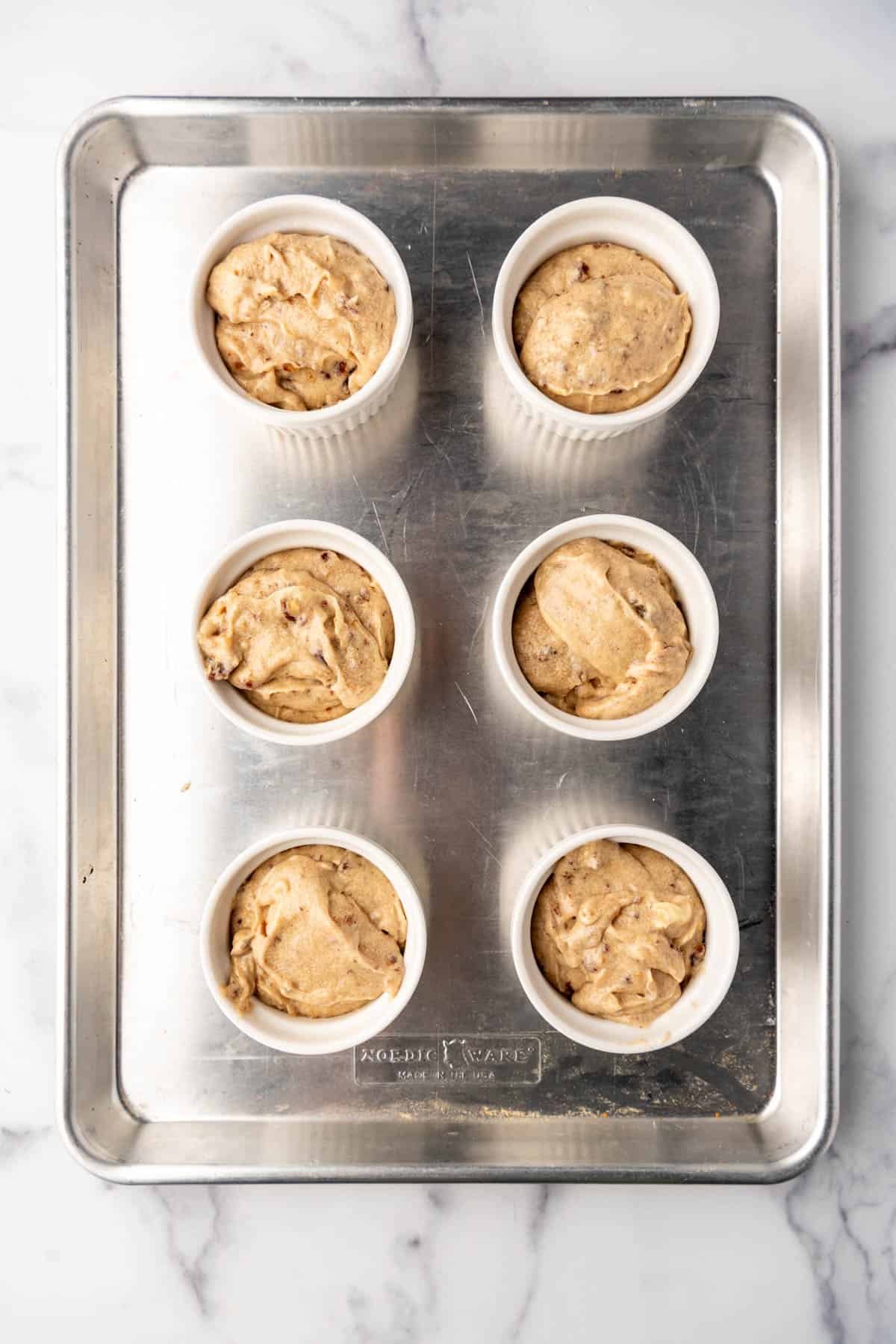 Cake batter in ramekins on a baking sheet.