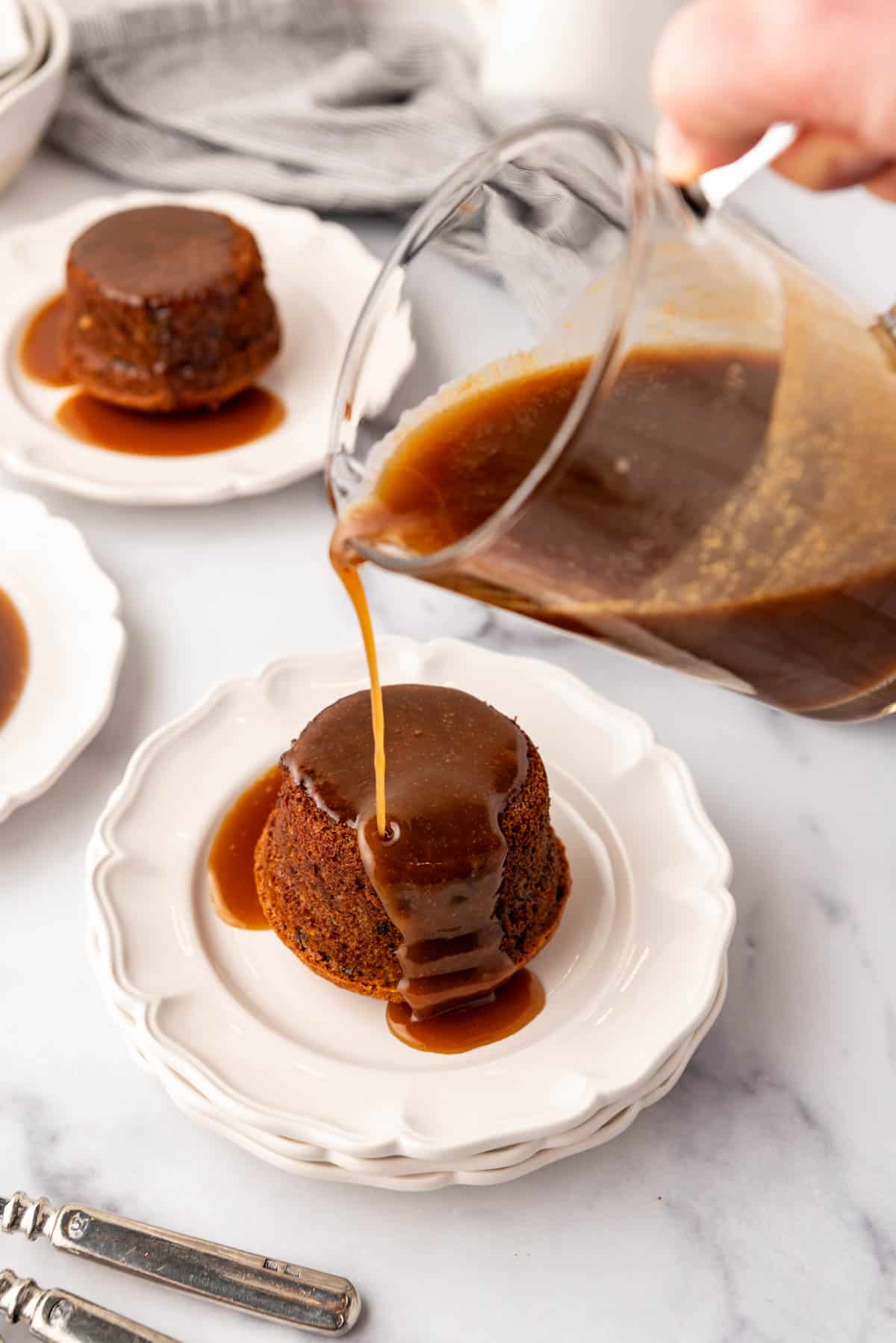 Pouring sticky toffee sauce over an individual cake on a dessert plate.