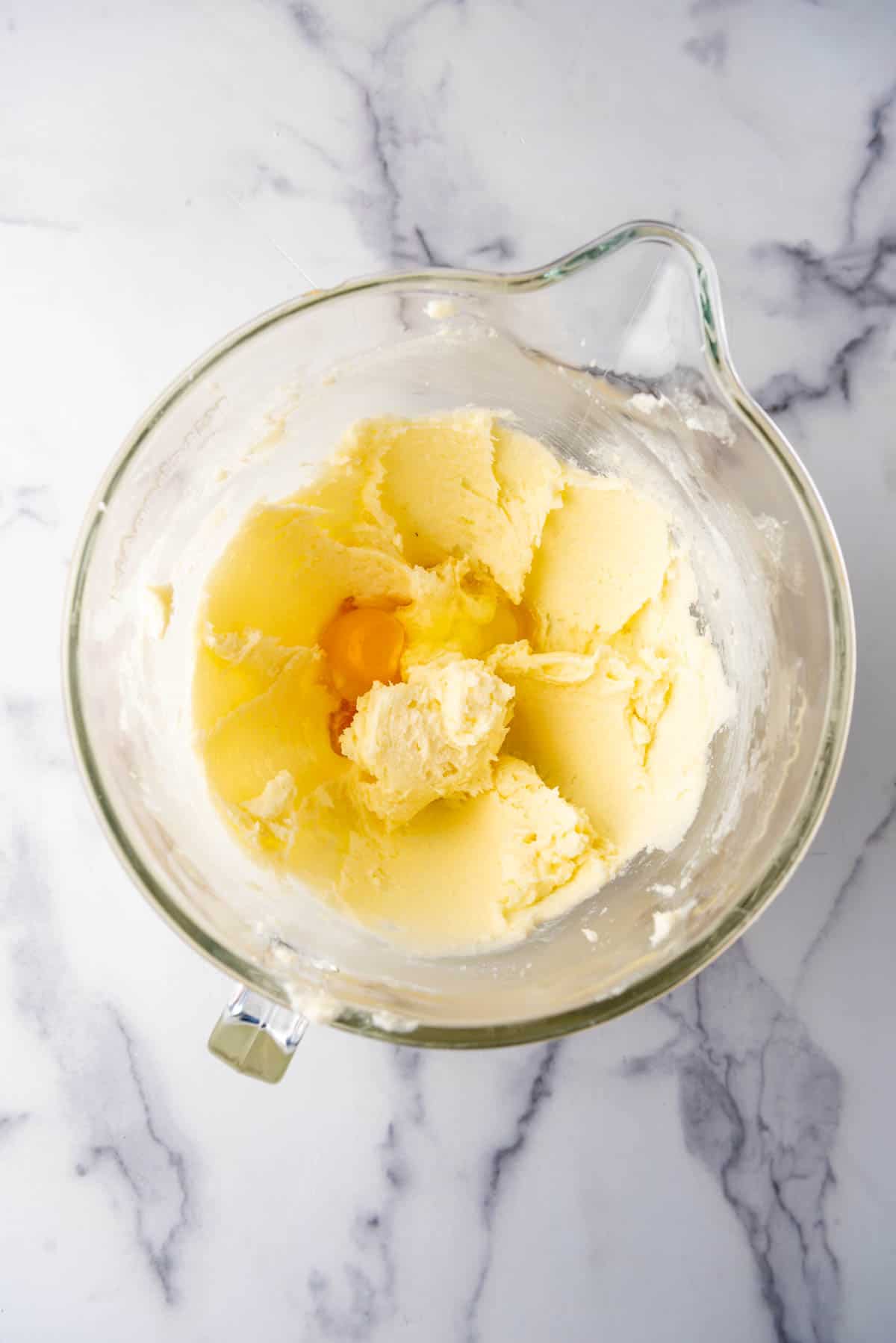 Adding an egg to creamed butter and sugar in a mixing bowl.