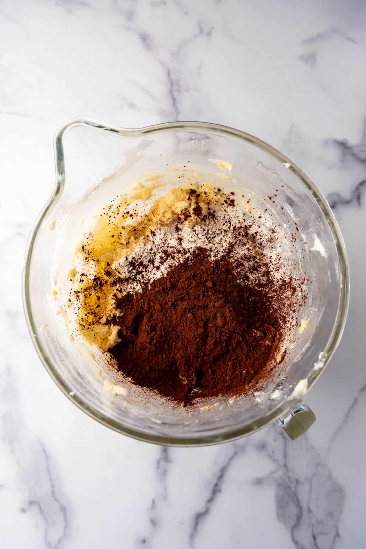 Adding dry ingredients like flour and dutch processed cocoa powder to creamed butter and sugar in a large mixing bowl.