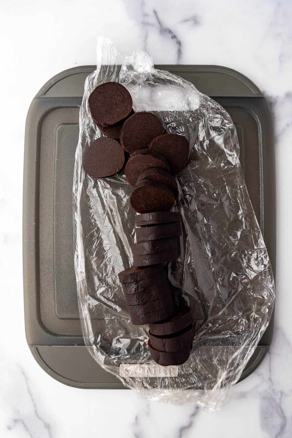 A sliced log of chocolate shortbread cookie dough on a cutting board.