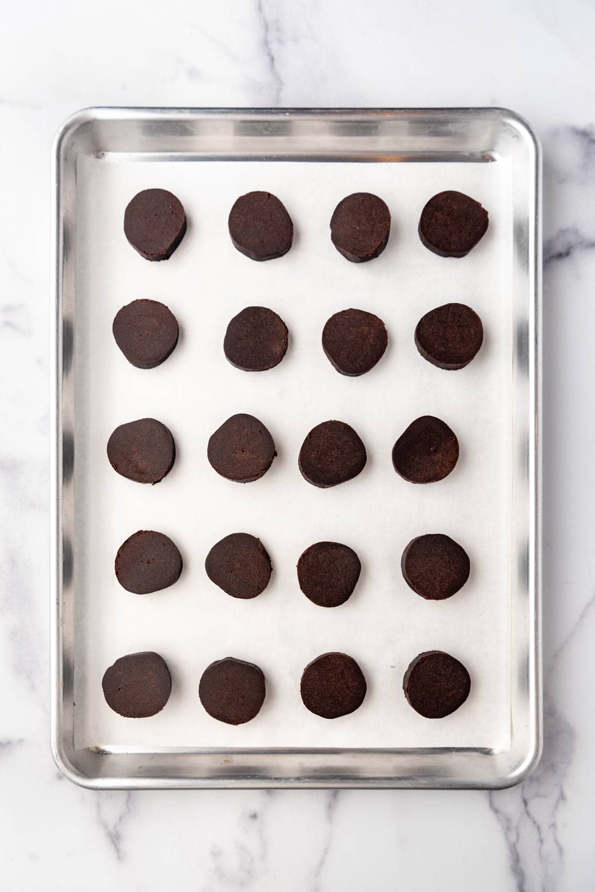 Circles of chocolate shortbread on a baking sheet lined with parchment paper ready to go in the oven.