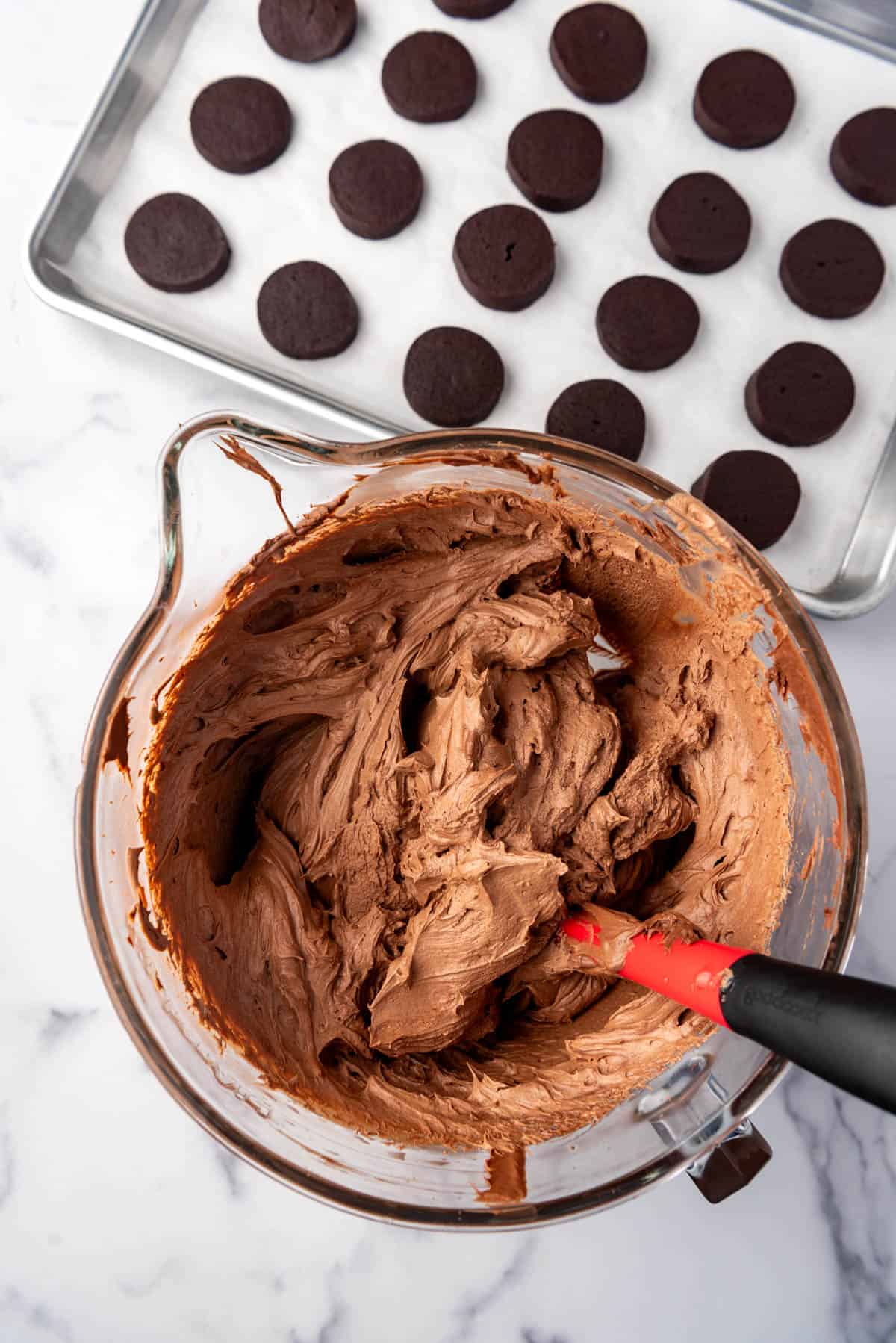 Whipped chocolate ganache in a mixing bowl with a red spatula.