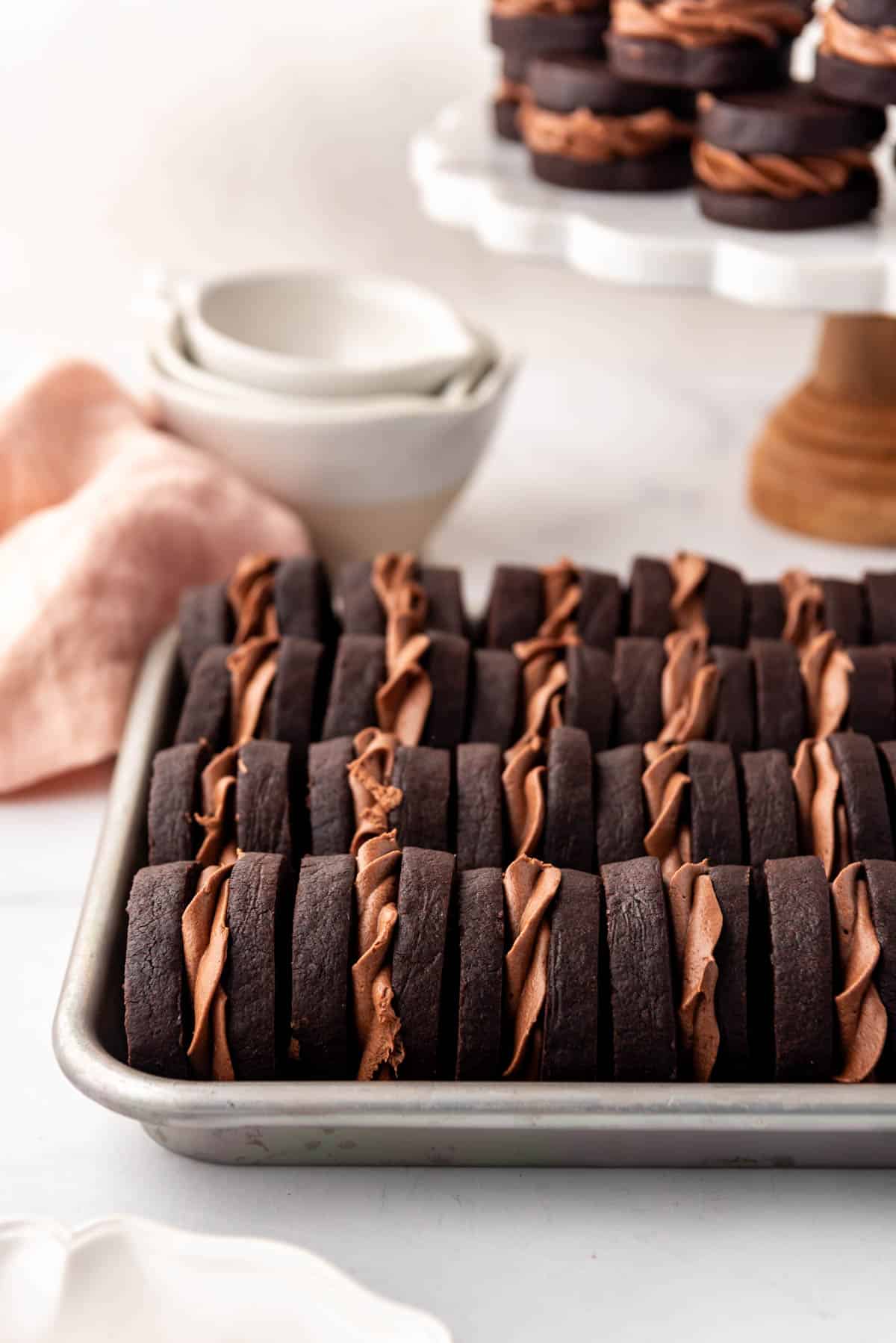 Rows of chocolate nutella sandwich cookies in front of more cookies on a cake stand.