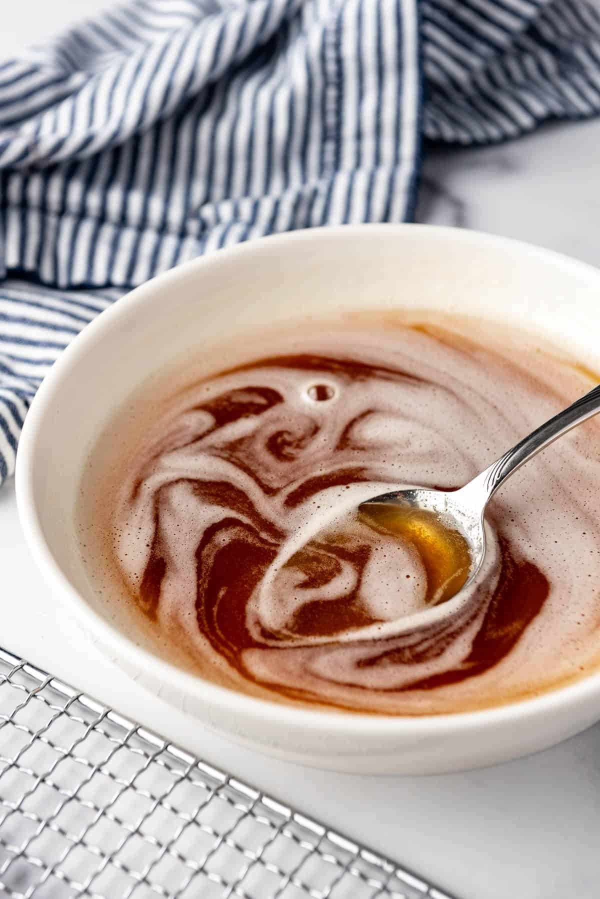 A spoon in a shallow white bowl of browned butter.