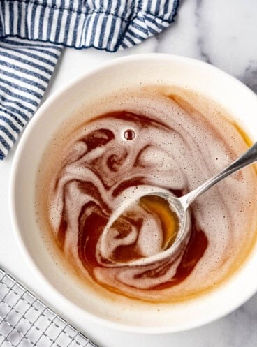 An overhead image of a bowl of brown butter with a spoon in it next to a striped cloth napkin and a wire rack.