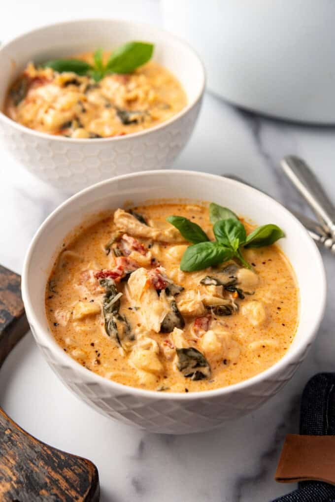 A side view of a bowl of creamy marry me chicken soup with basil garnish.