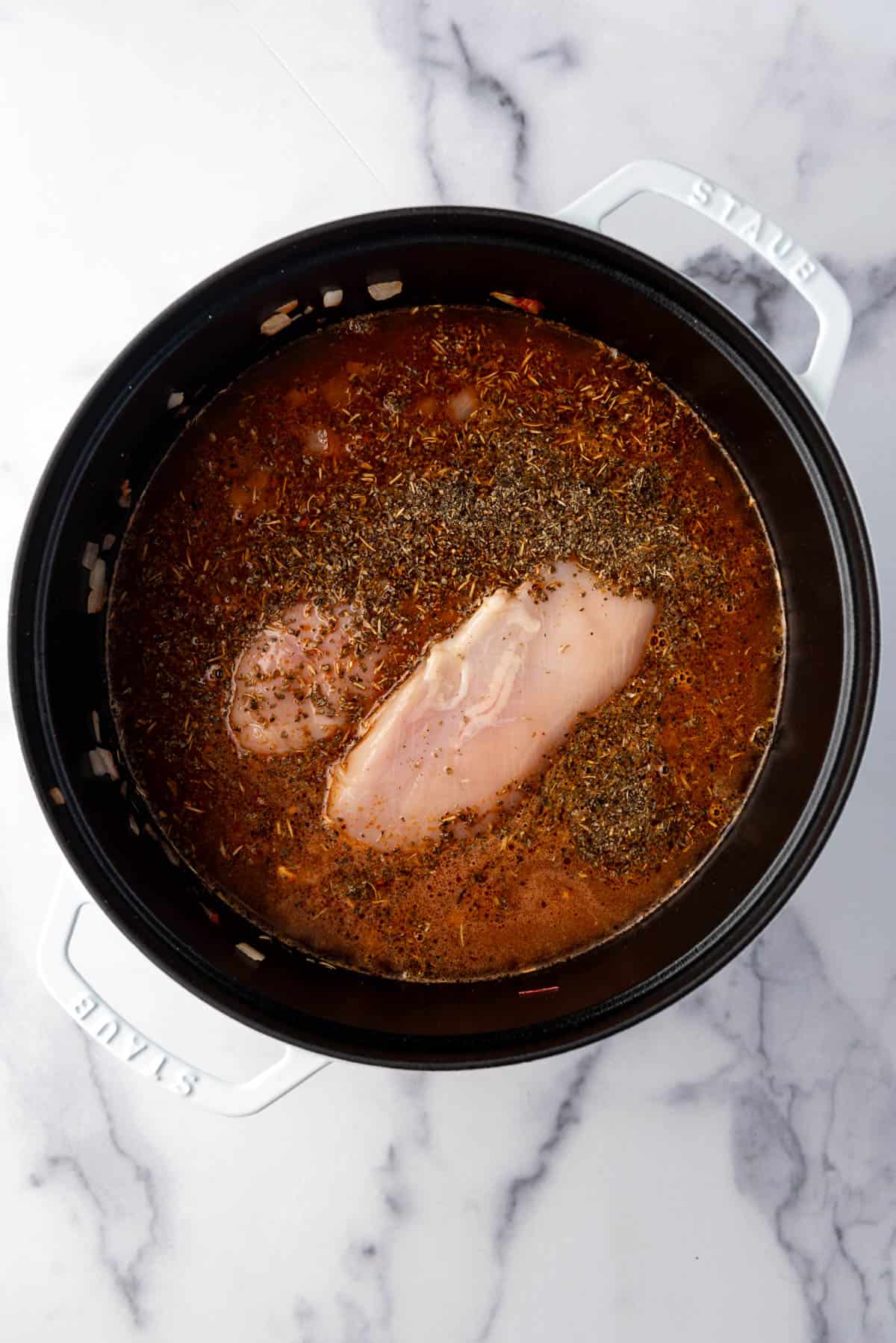 Adding chicken breasts, spices, and chicken broth to a large dutch oven to make soup.