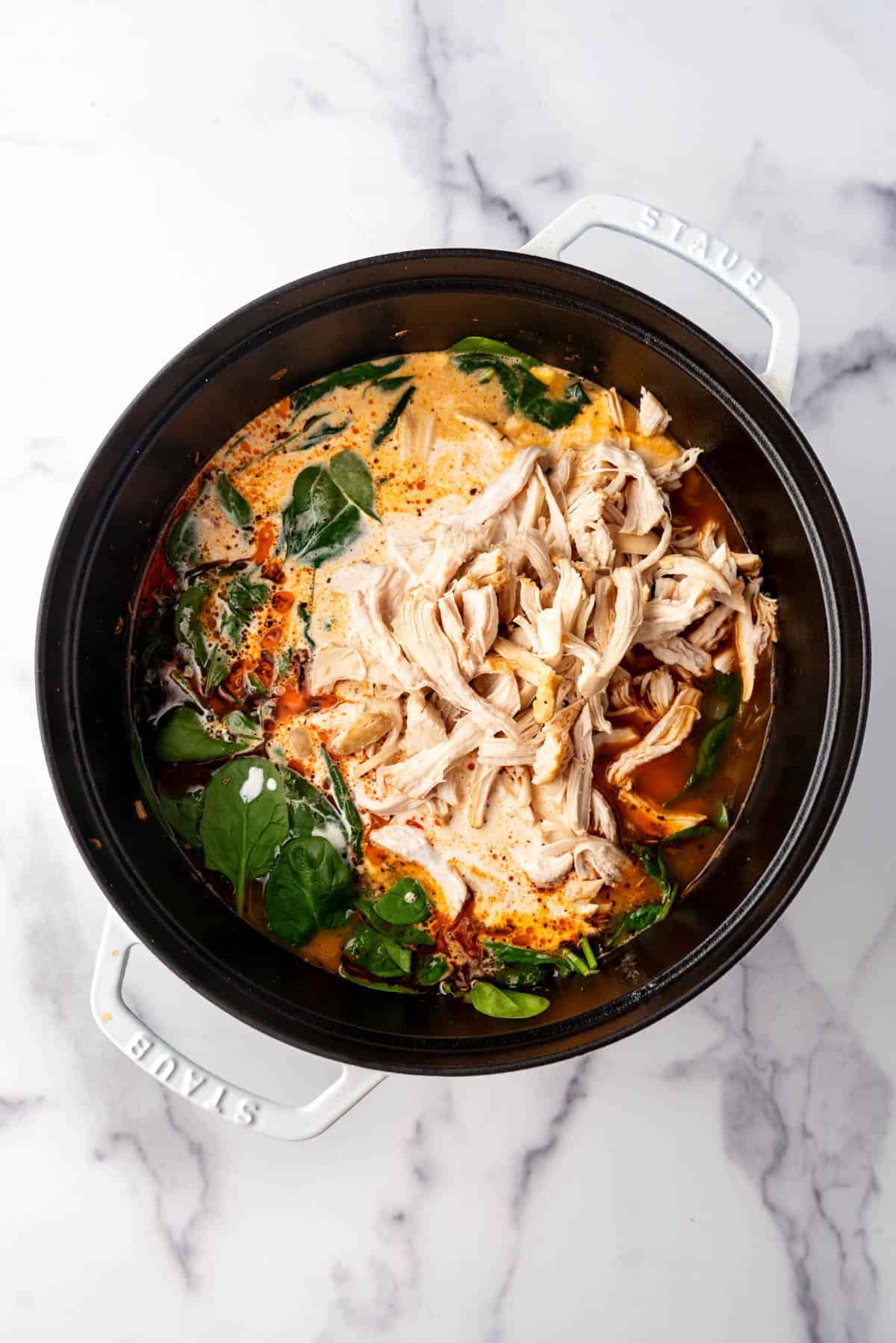 Adding shredded chicken, spinach, and cream to a pot of soup.