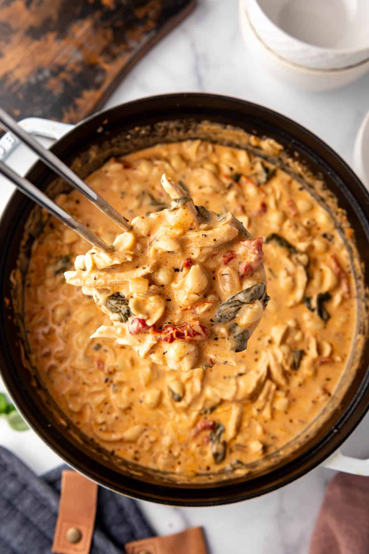 An overhead image of a ladleful of marry me chicken soup being lifted out of the pot.