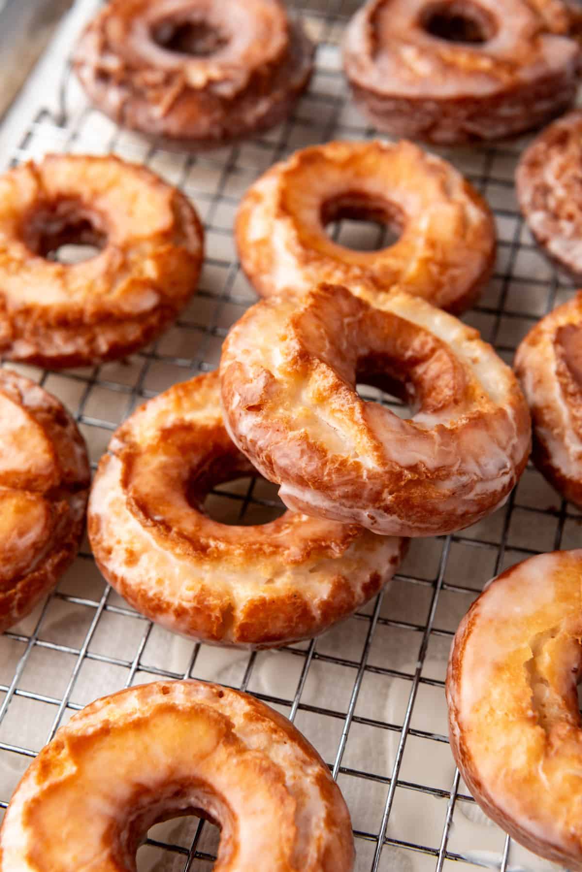 Two glazed old-fashioned donuts partially stacked next to more doughnuts.