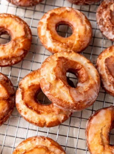 An image of two donuts stacked on top of each other next to more donuts on a wire rack.