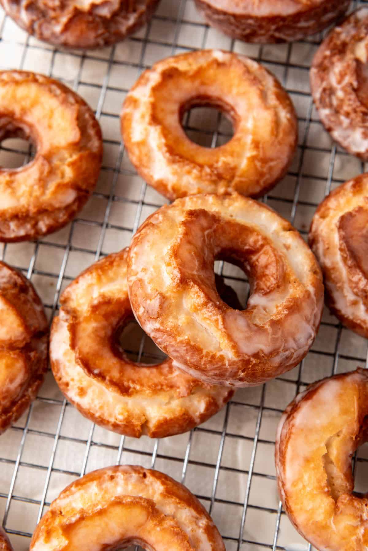 An image of two donuts stacked on top of each other next to more donuts on a wire rack.