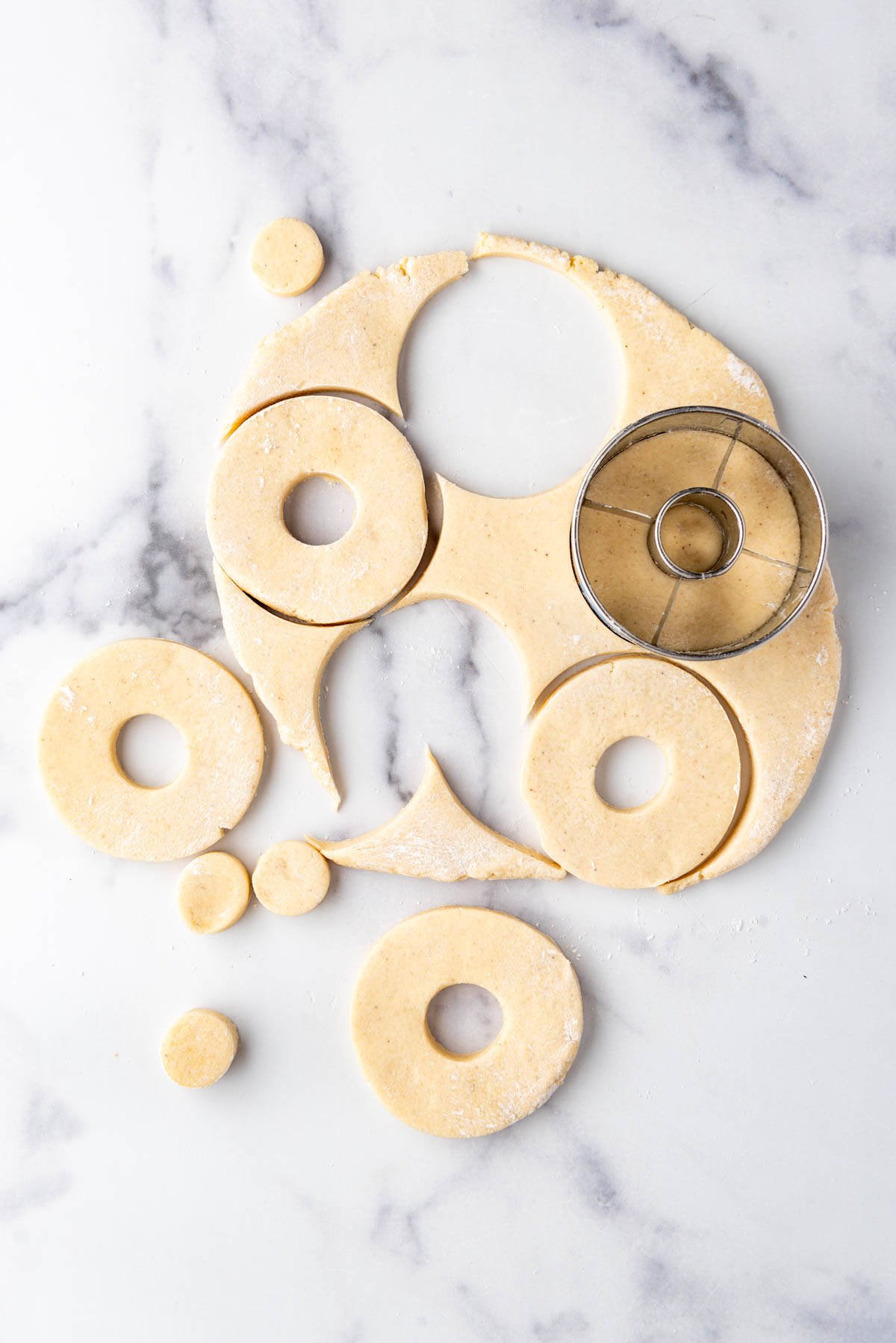 Cutting doughnuts out on a white marble surface using a donut cutter.