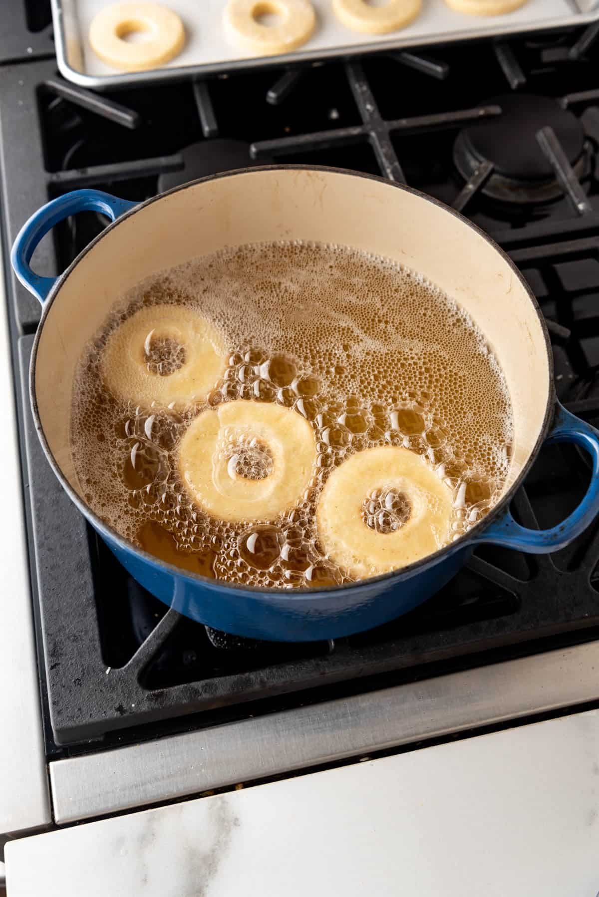 An image of three doughnuts frying in hot oil on a stovetop.