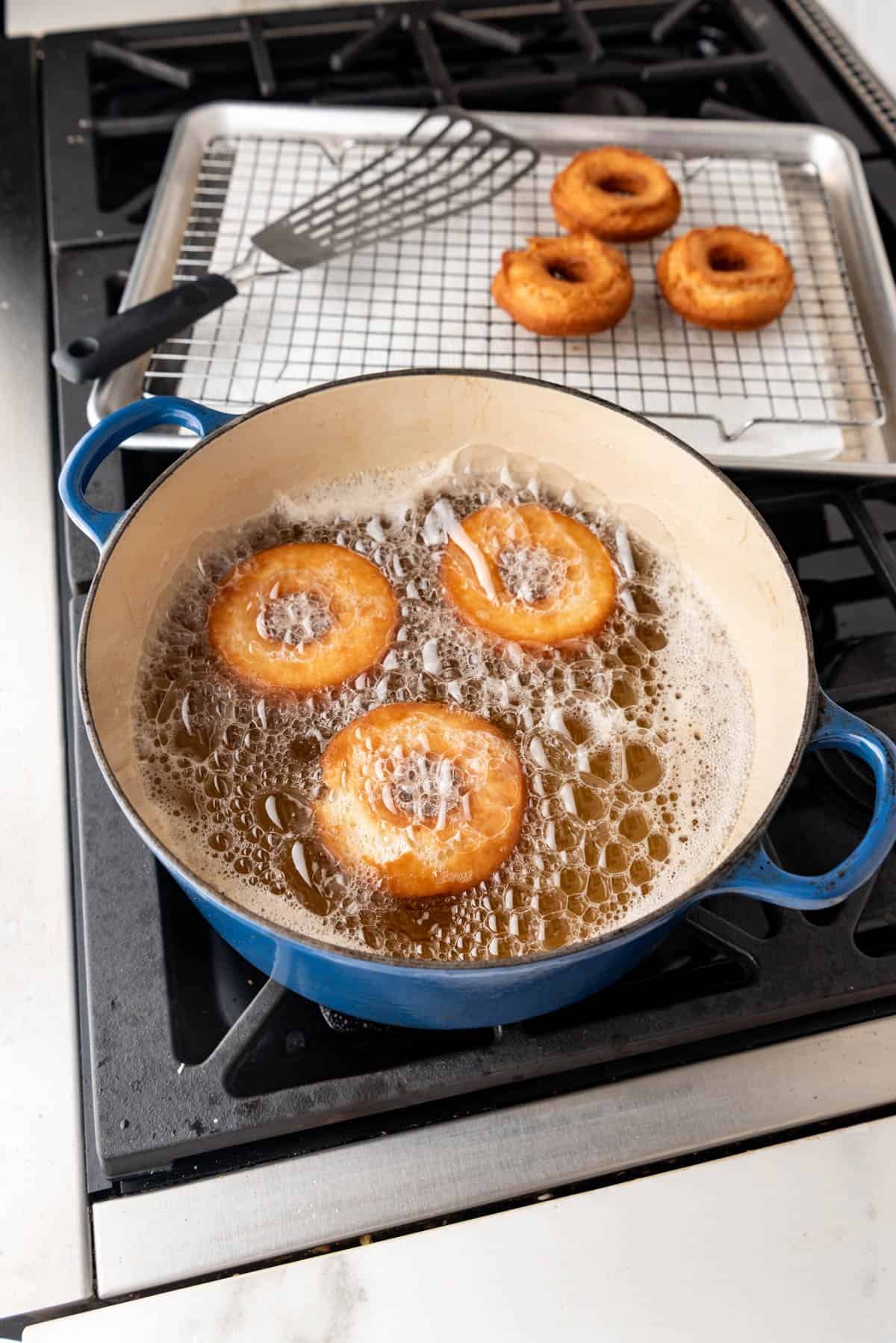 Doughnuts frying in hot oil in a large dutch oven.