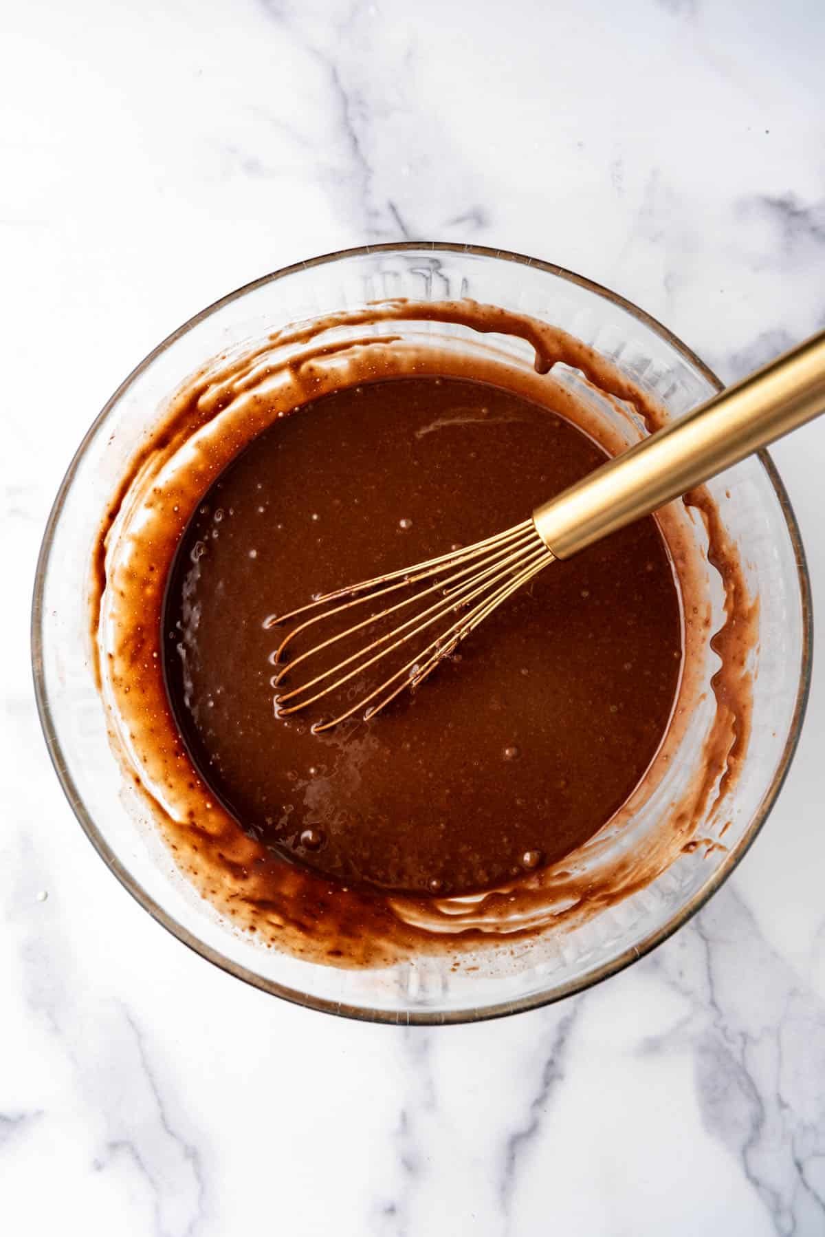 Chocolate cake batter in a mixing bowl with a whisk in it.