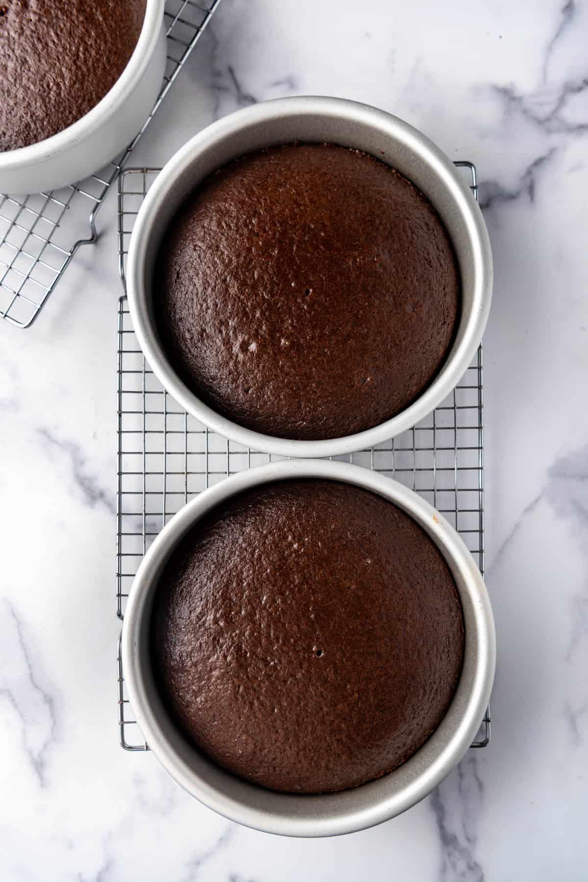 Chocolate cake layers cooling in their pans on a wire rack.