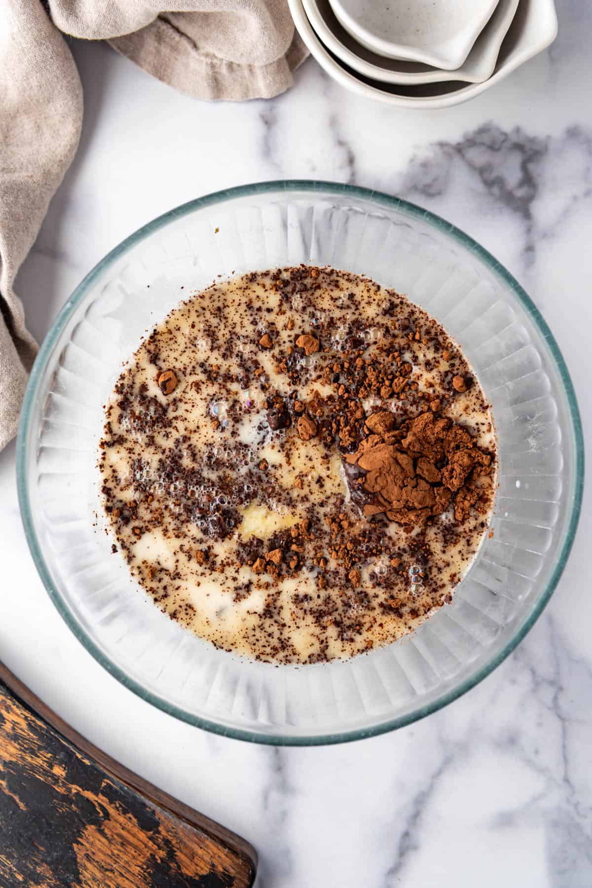 Combining hot cream, melted butter, chocolate chips, and cocoa powder in a mixing bowl.