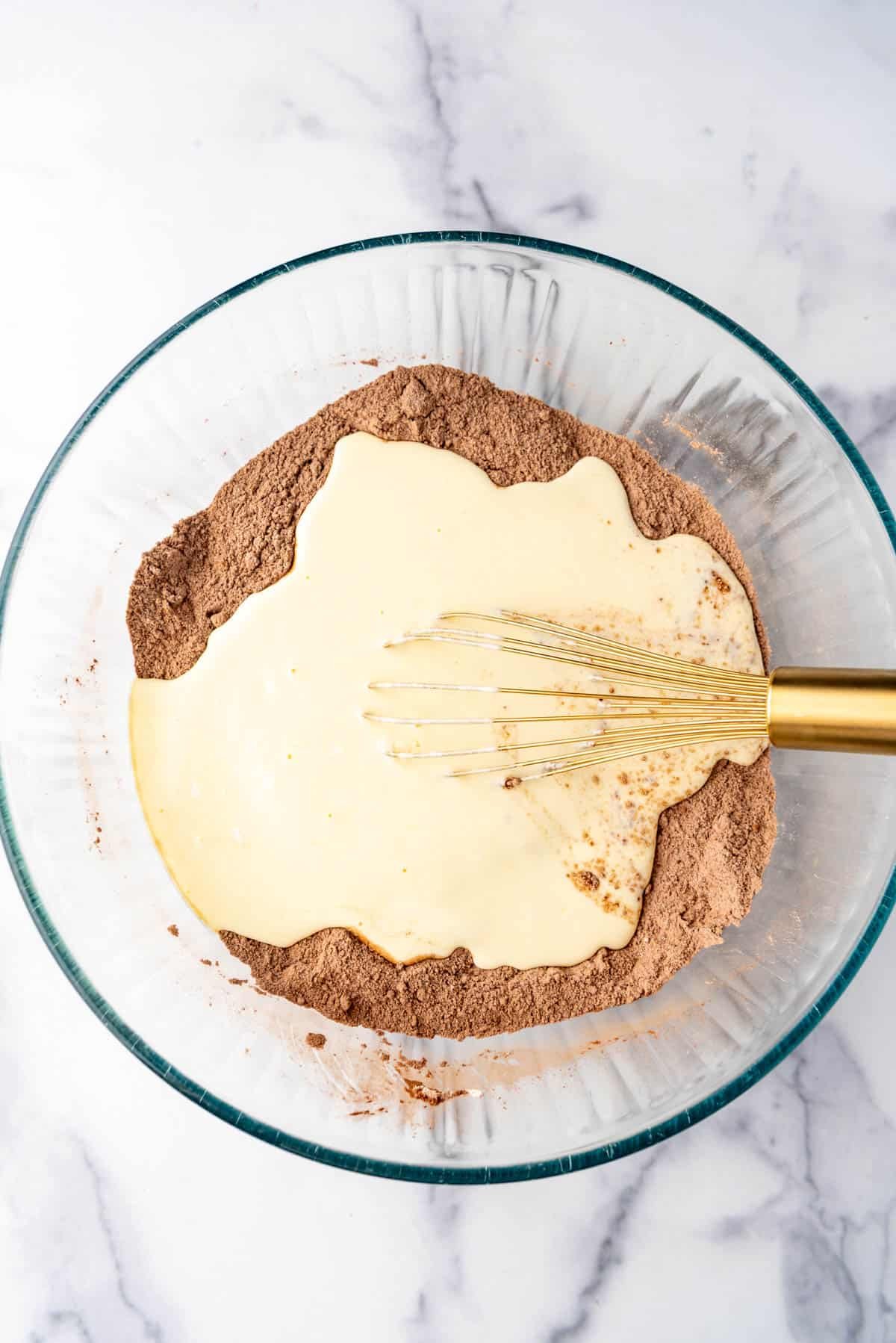 Adding  wet ingredients to dry ingredients in a bowl with a whisk.