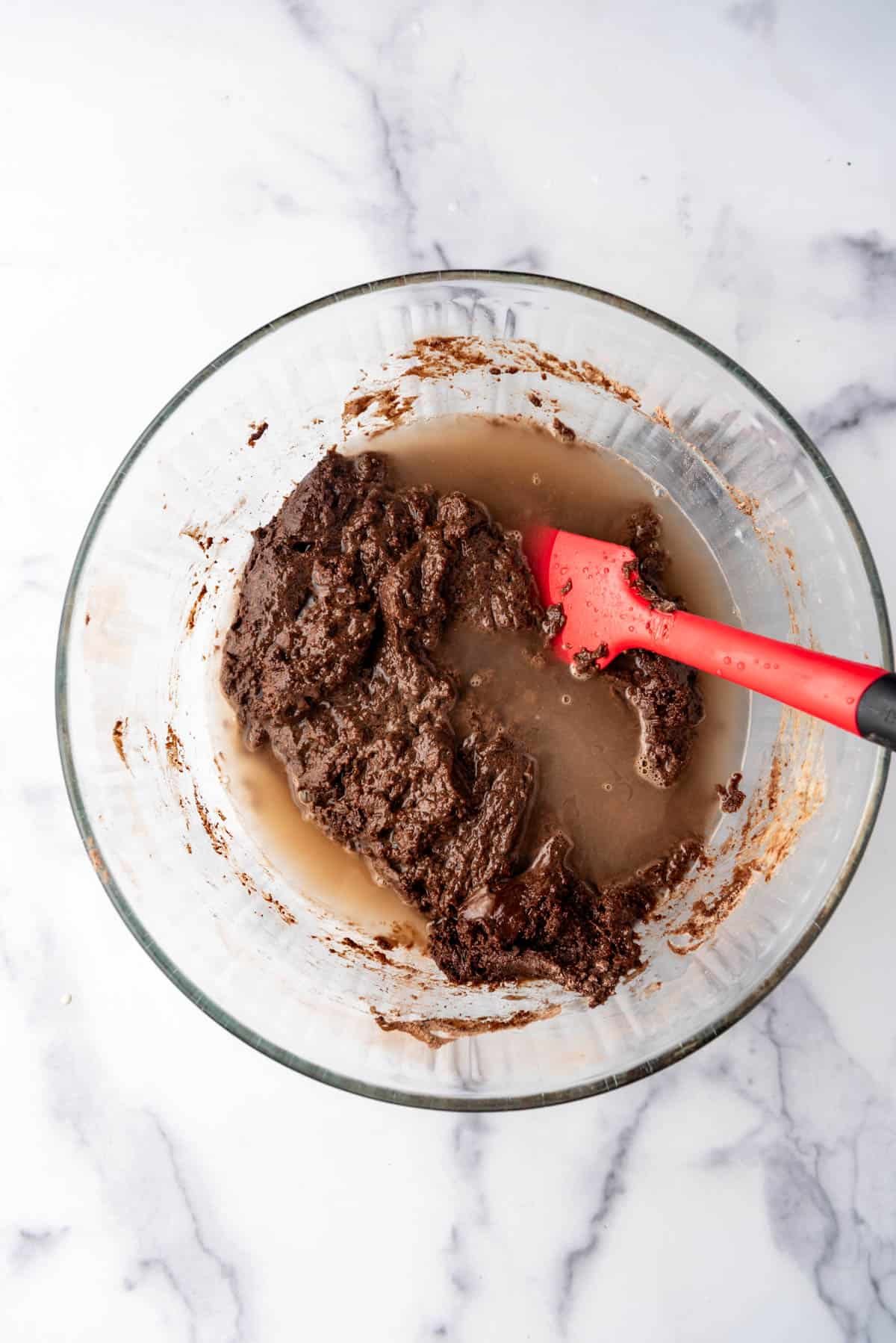 Adding hot water to chocolate cake batter in a mixing bowl with a red spatula.