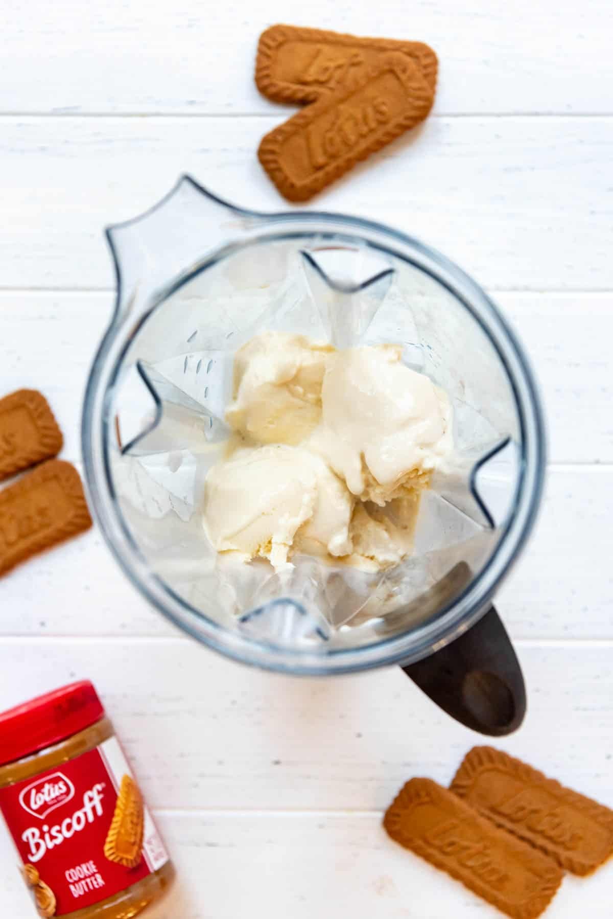 Blending vanilla ice cream and milk in a blender with Biscoff cookies and a jar of cookie butter spread nearby.