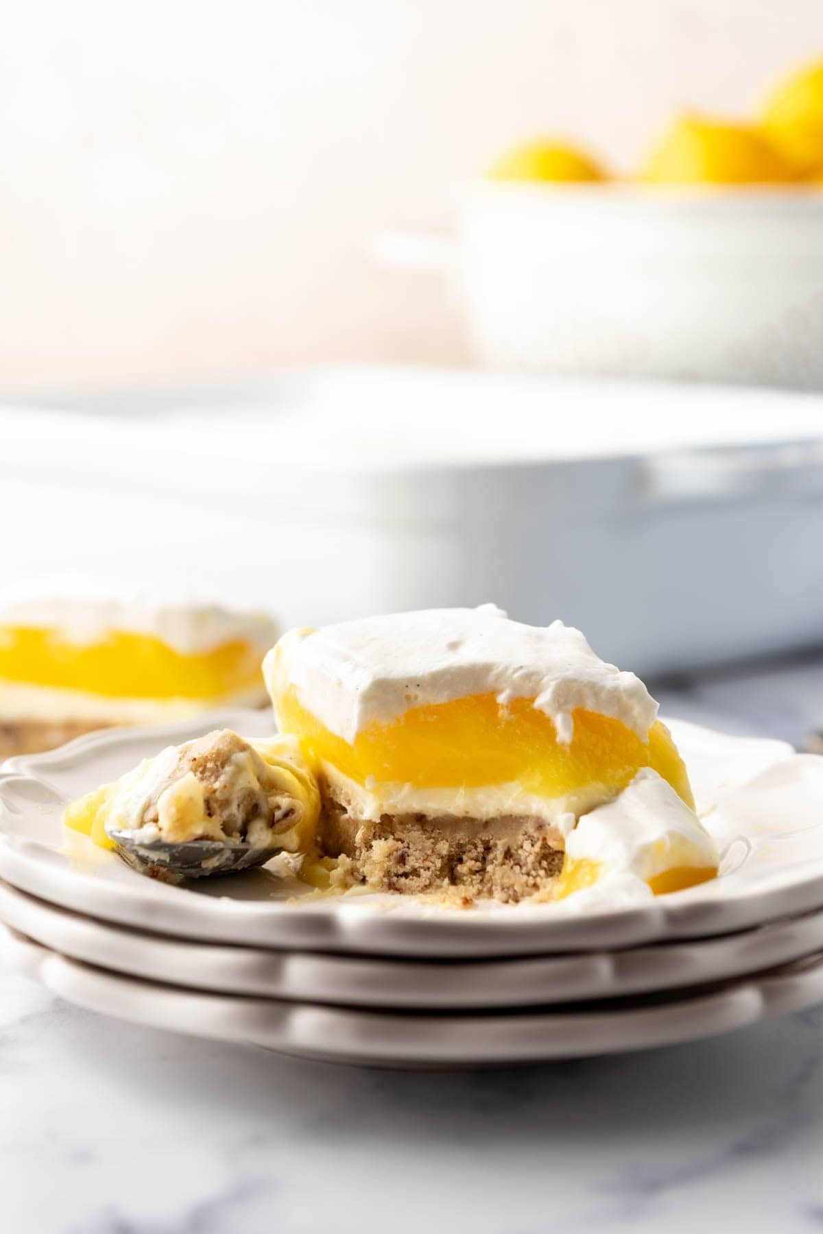 A stack of plates with lemon lush dessert on it with a bite taken out of it.
