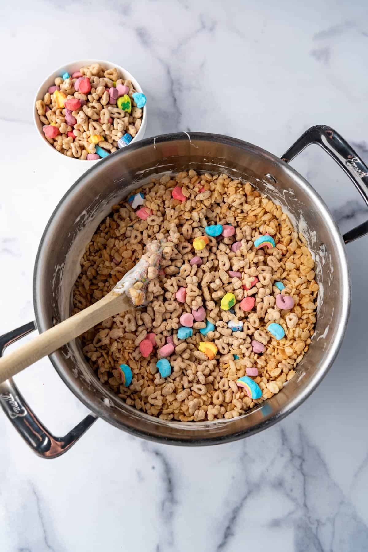 Adding Lucky Charms and Rice Krispies to a pot of melted marshmallows.