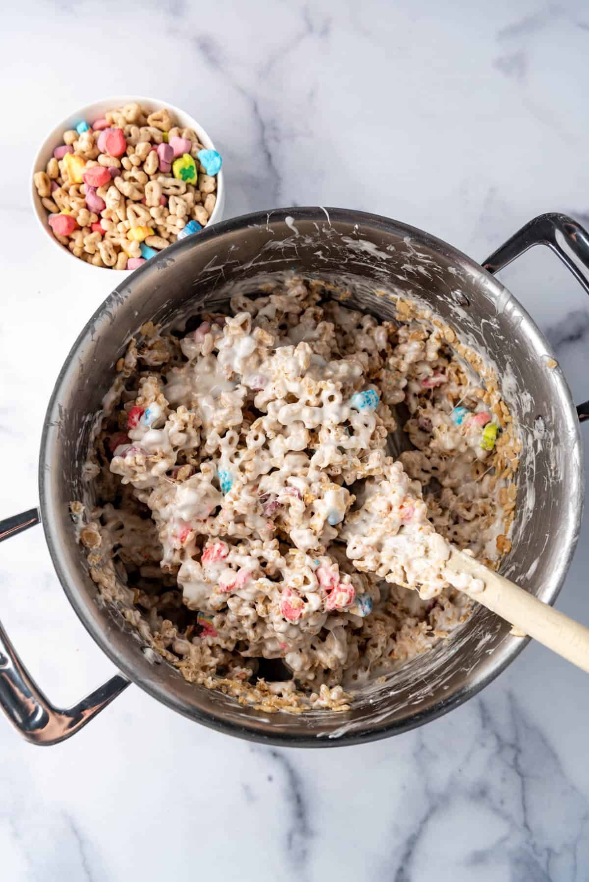 Stirring cereal into melted marshmallows for Lucky Charms cereal treats.