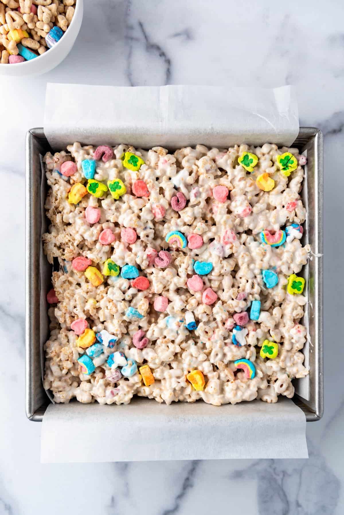 Lucky Charms cereal treats that have been pressed into a square pan lined with parchment paper.